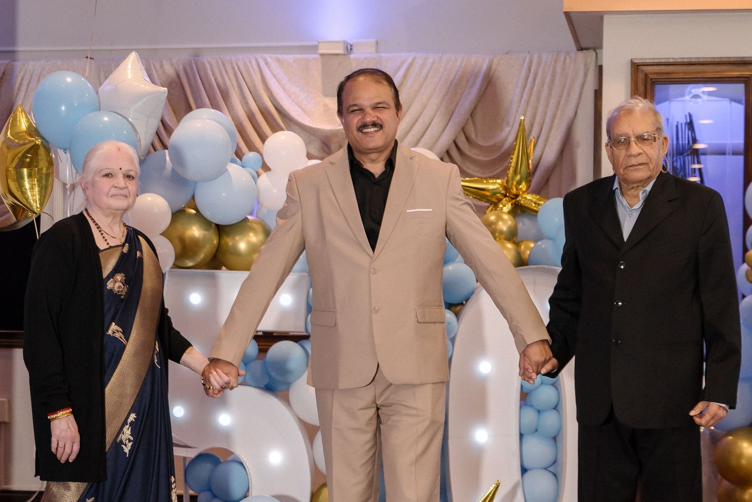 A group of people celebrate at an elegant party with gold and blue balloon decorations and curtains.