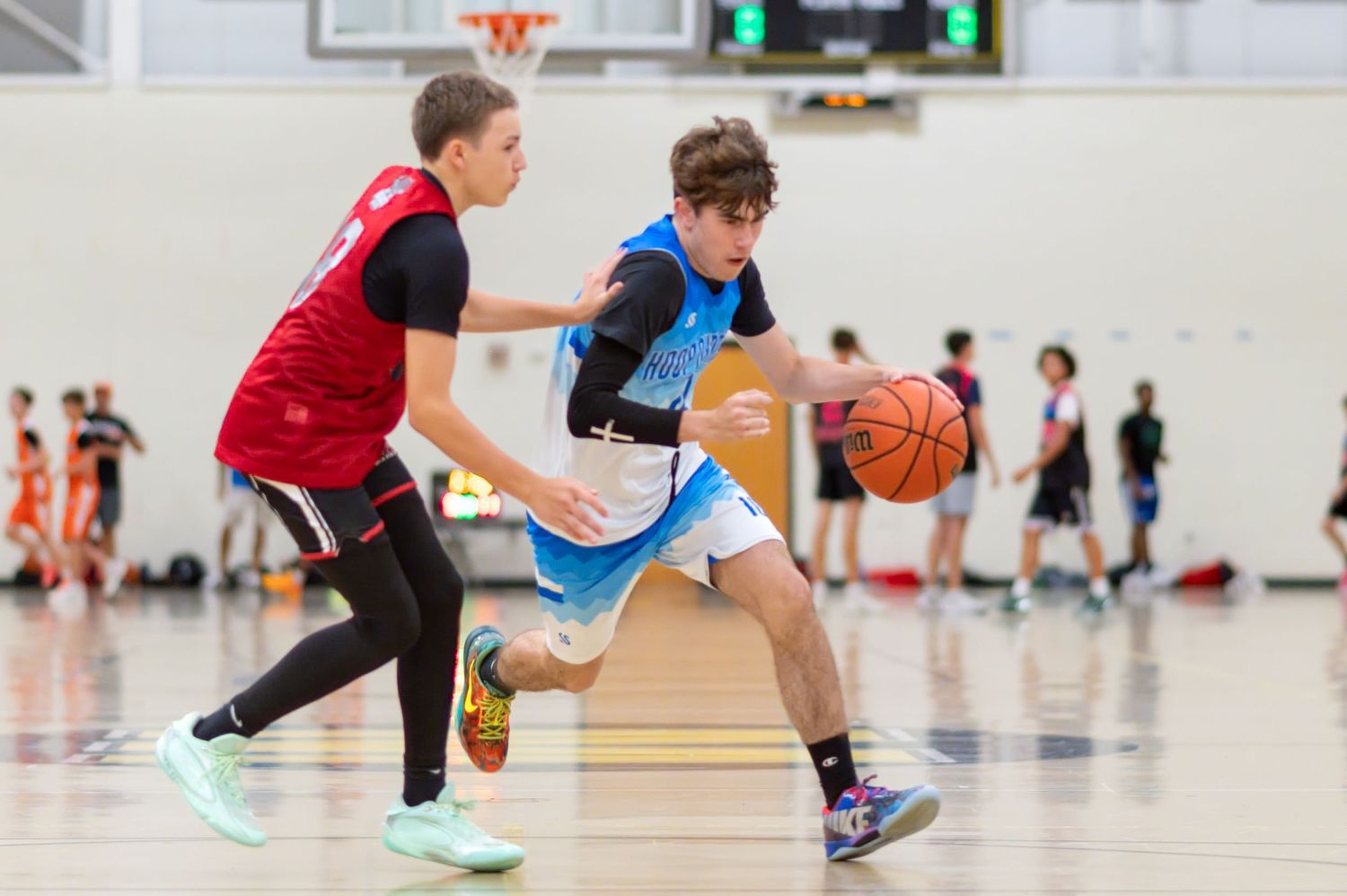 Two young basketball players compete on an indoor court, one dribbling past a defender during a youth basketball game.