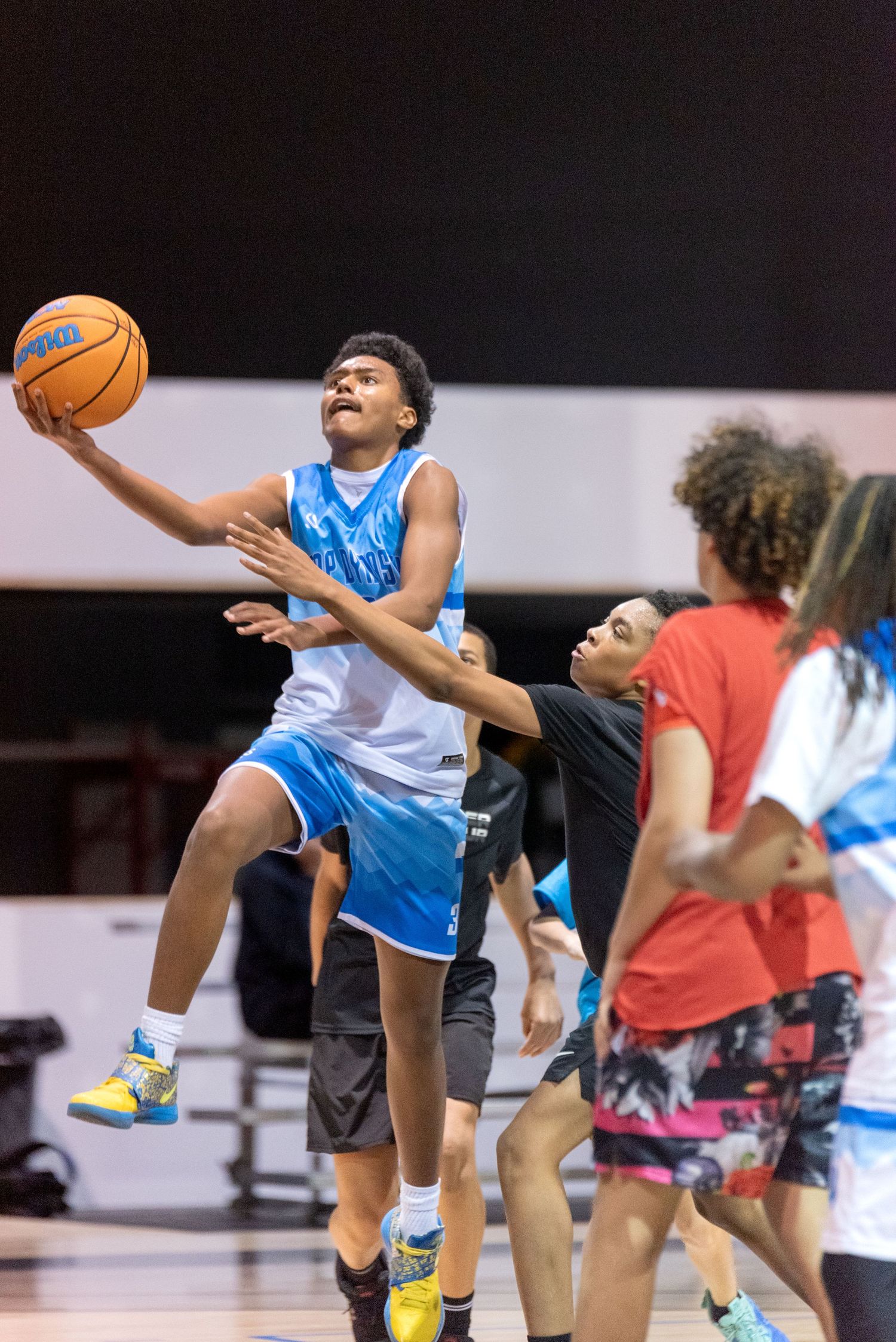 Young basketball player in blue uniform leaps for a layup during an intense youth basketball game indoors.