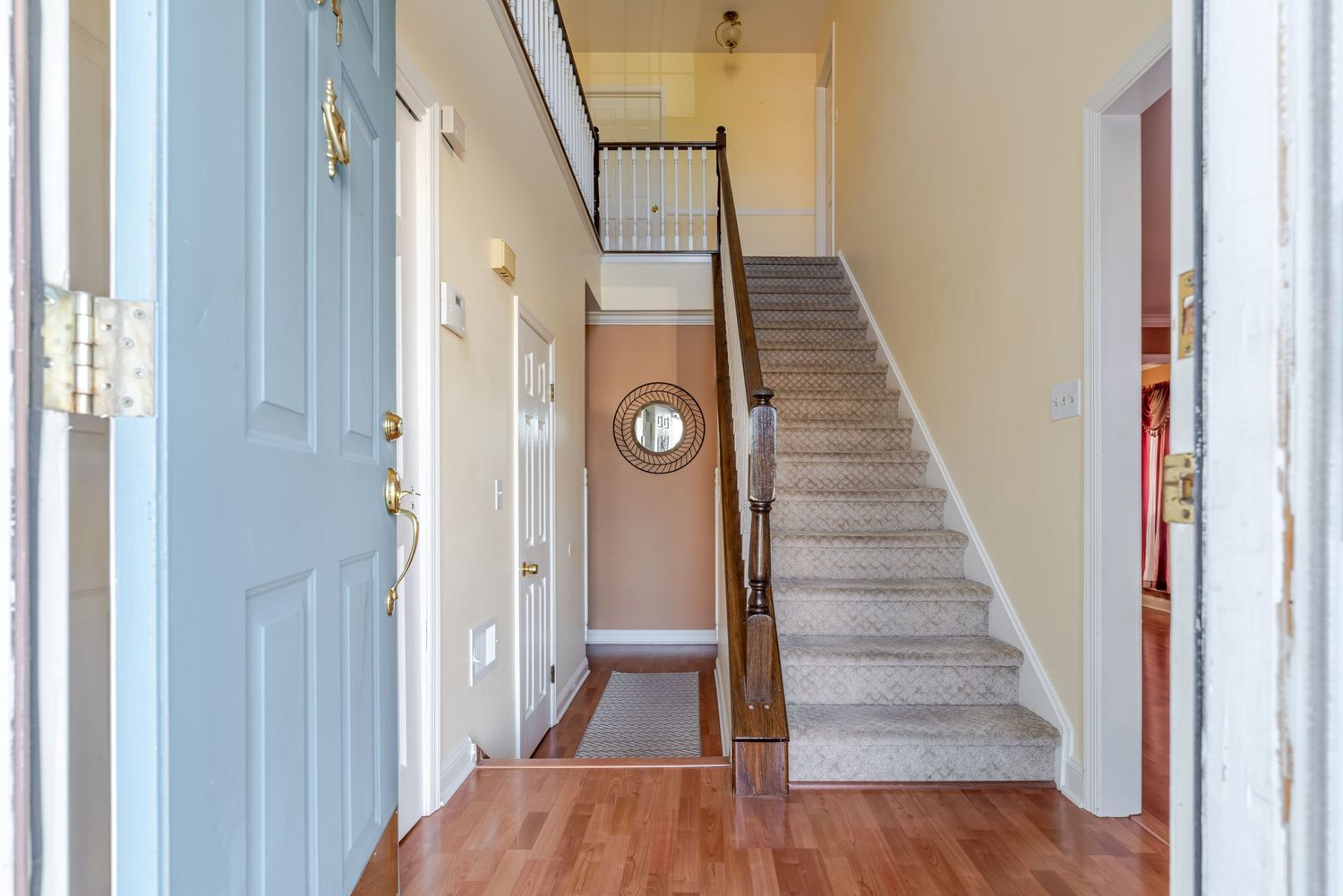 Bright entryway with hardwood floors, carpeted staircase, white doors, and neutral walls in a welcoming home foyer.