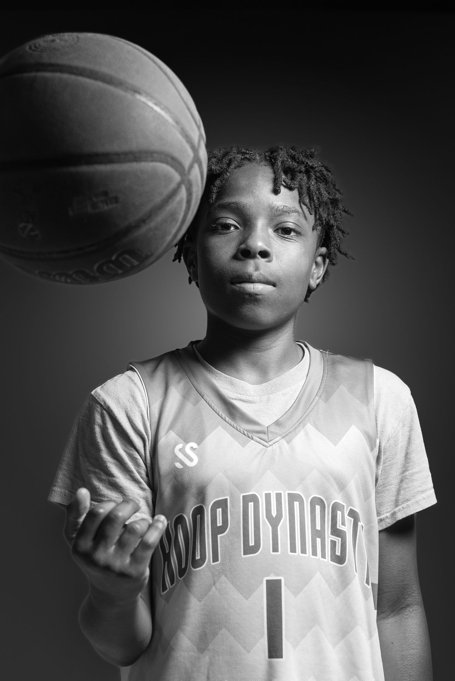 Black and white portrait of a young basketball player in a Hoop Dynasty jersey tossing a basketball.