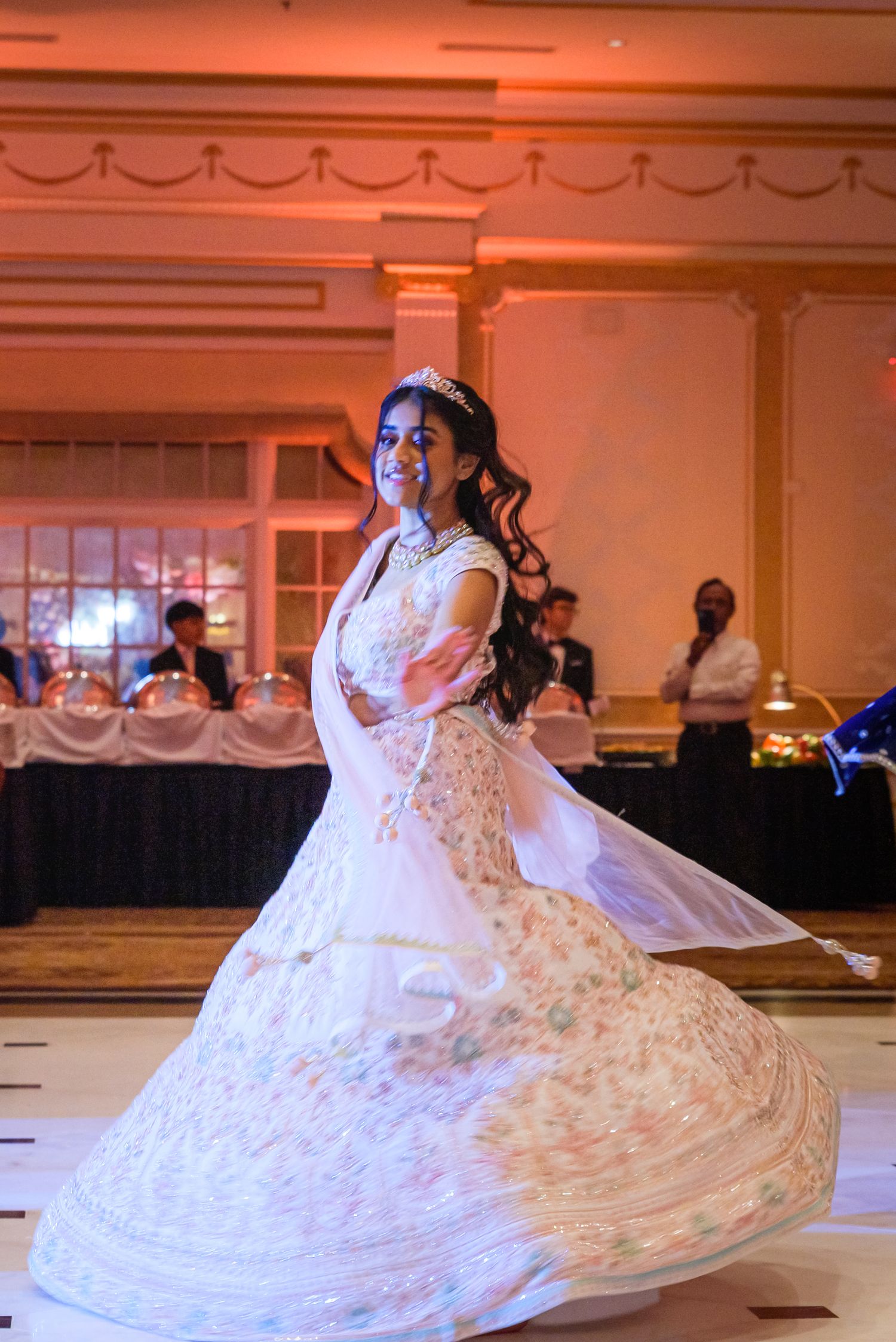 Performer in an elaborate white dress twirling during a wedding dance performance.