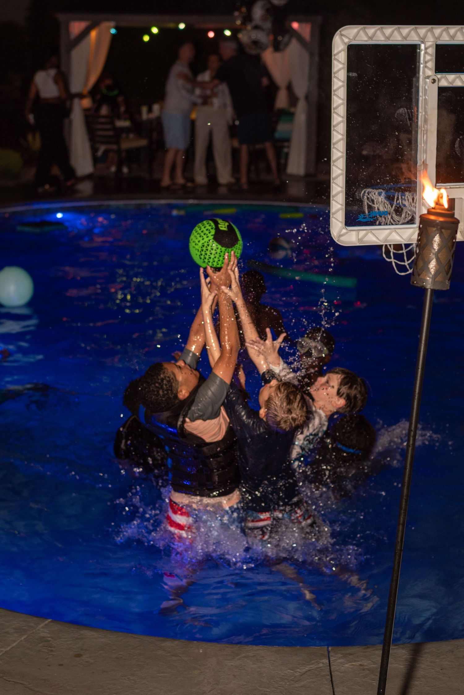 People splashing and playing in a pool during a nighttime swimming event.
