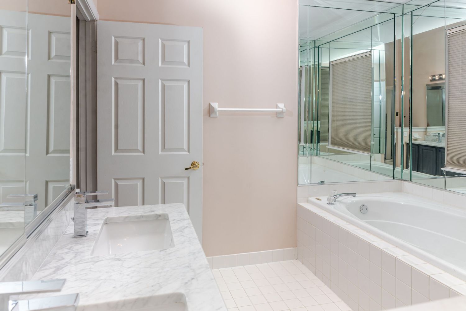 Bright bathroom featuring marble countertop, soaking tub, mirrored walls, and white tile flooring.