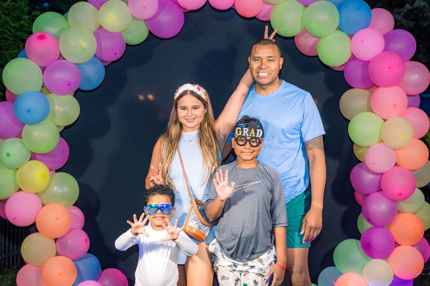 A festive celebration with colorful balloon arches and groups of people posing together.