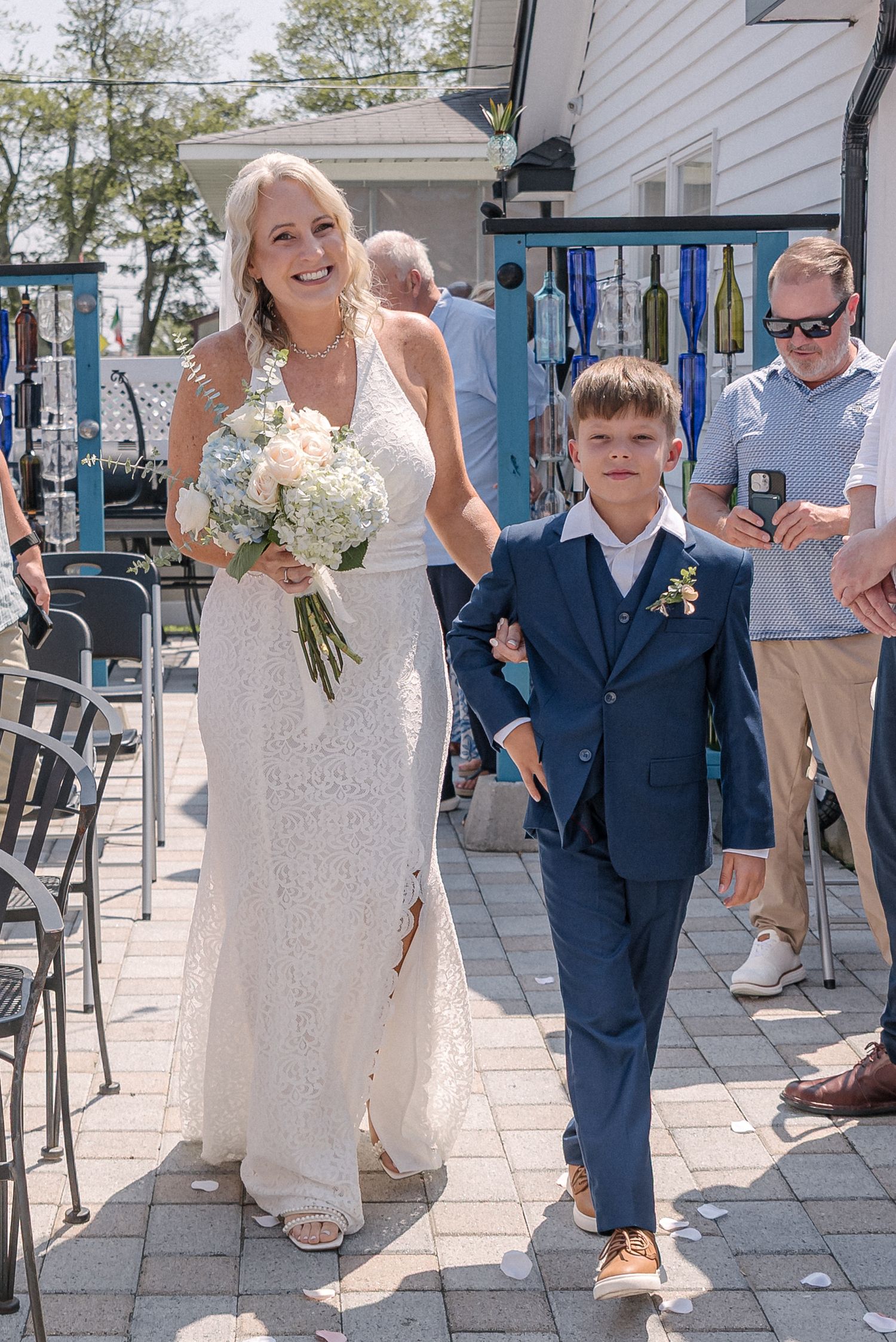 Wedding party walking on outdoor patio with white floral bouquet and navy blue suits.