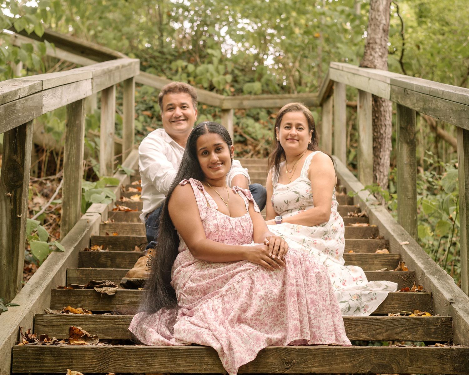A group in coordinating pink floral dresses poses together on wooden steps in a natural outdoor setting.