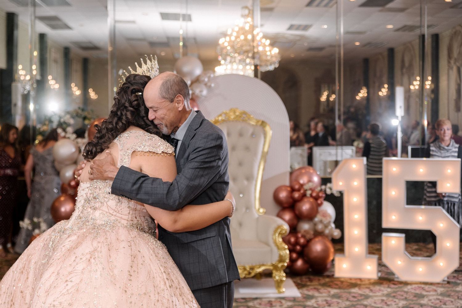 Ballroom decorated with rose gold balloons and chandeliers for a special celebration.