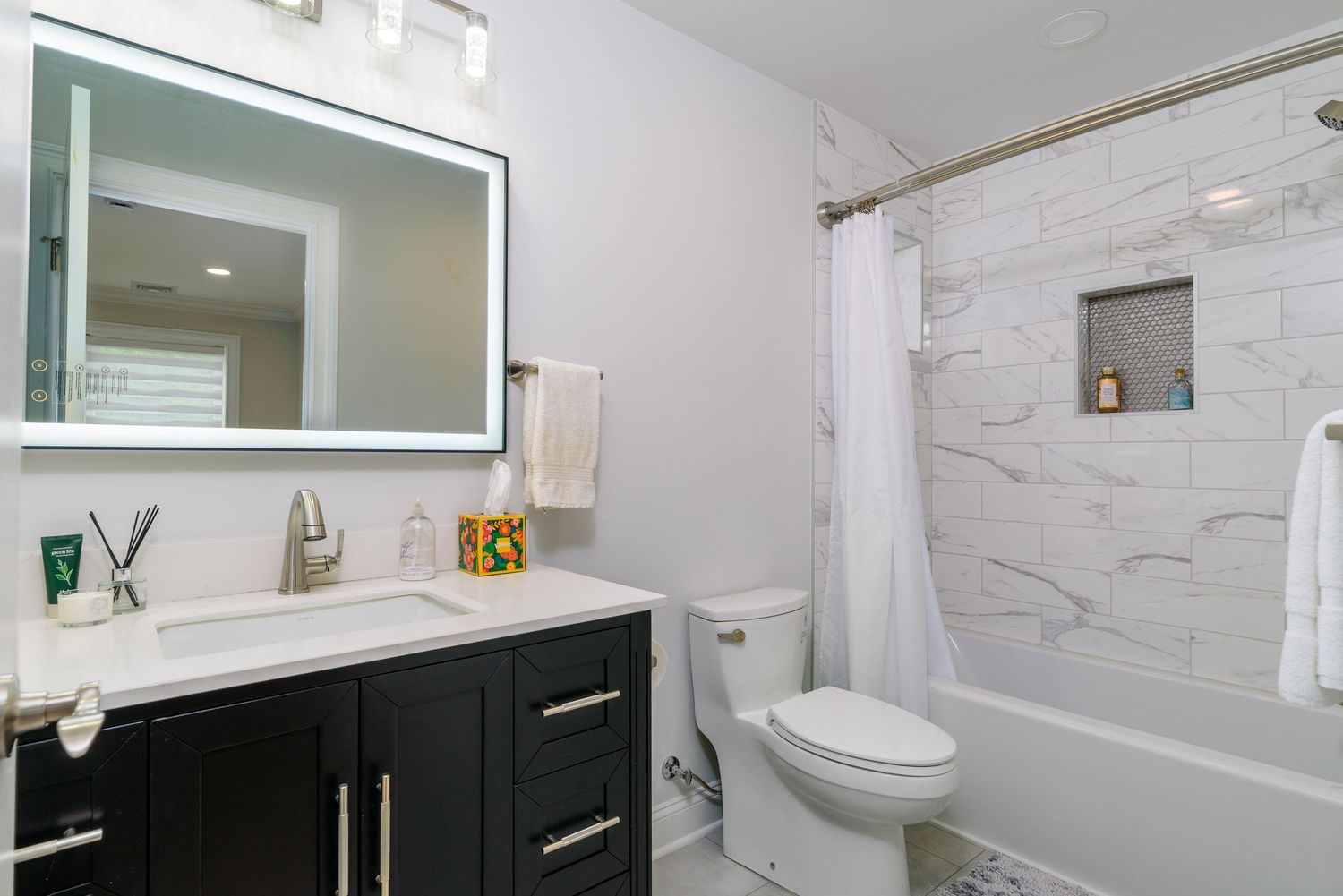 Contemporary bathroom featuring white marble tiles, black vanity, and modern fixtures.