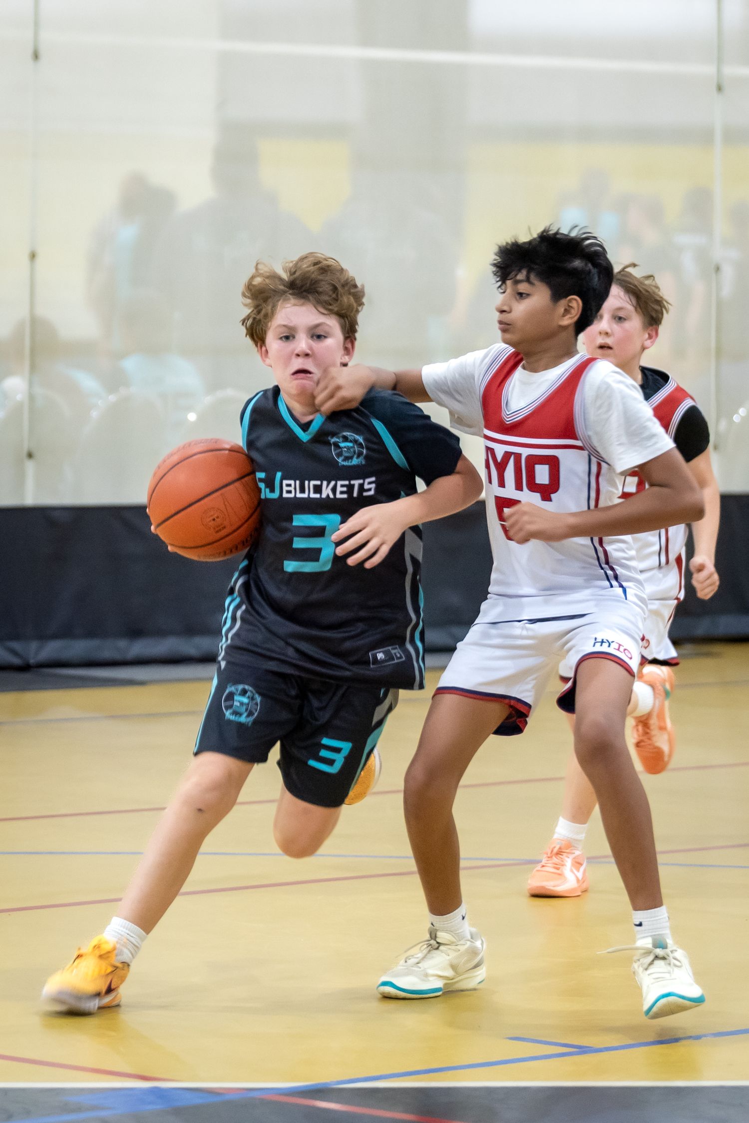 Youth basketball player number 3 in teal SJ Buckets jersey dribbles past defender in indoor game.