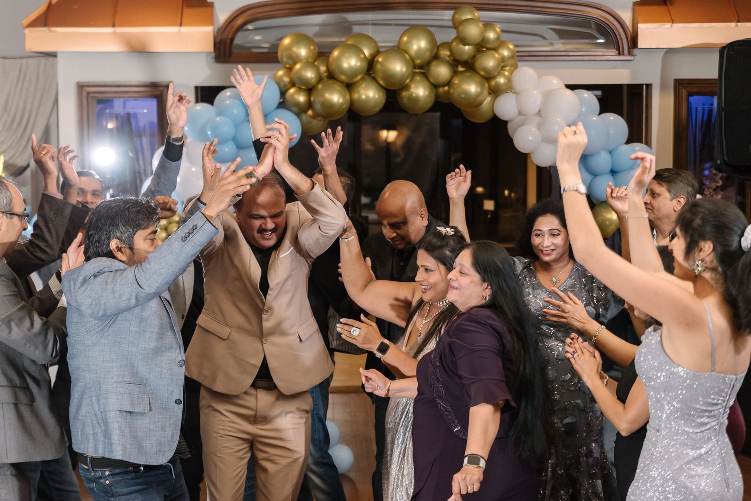 Celebration scene with people dancing and having fun under gold and blue balloon decorations.