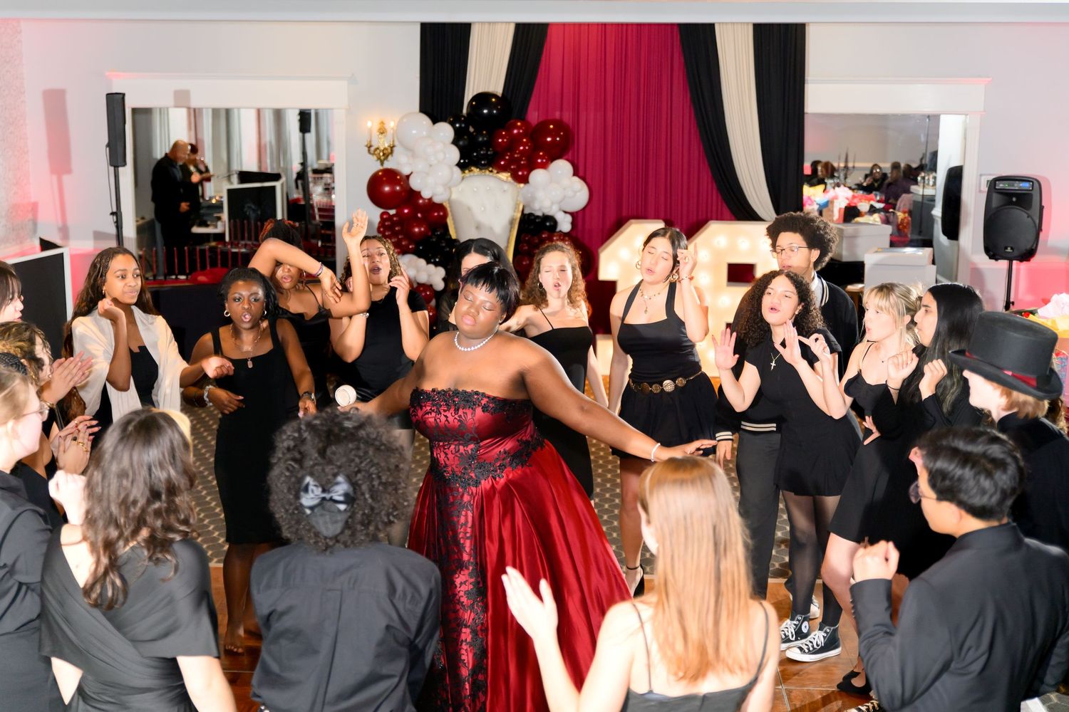 Guests dancing joyfully at an elegant red and black themed party with balloon decorations and festive lighting.