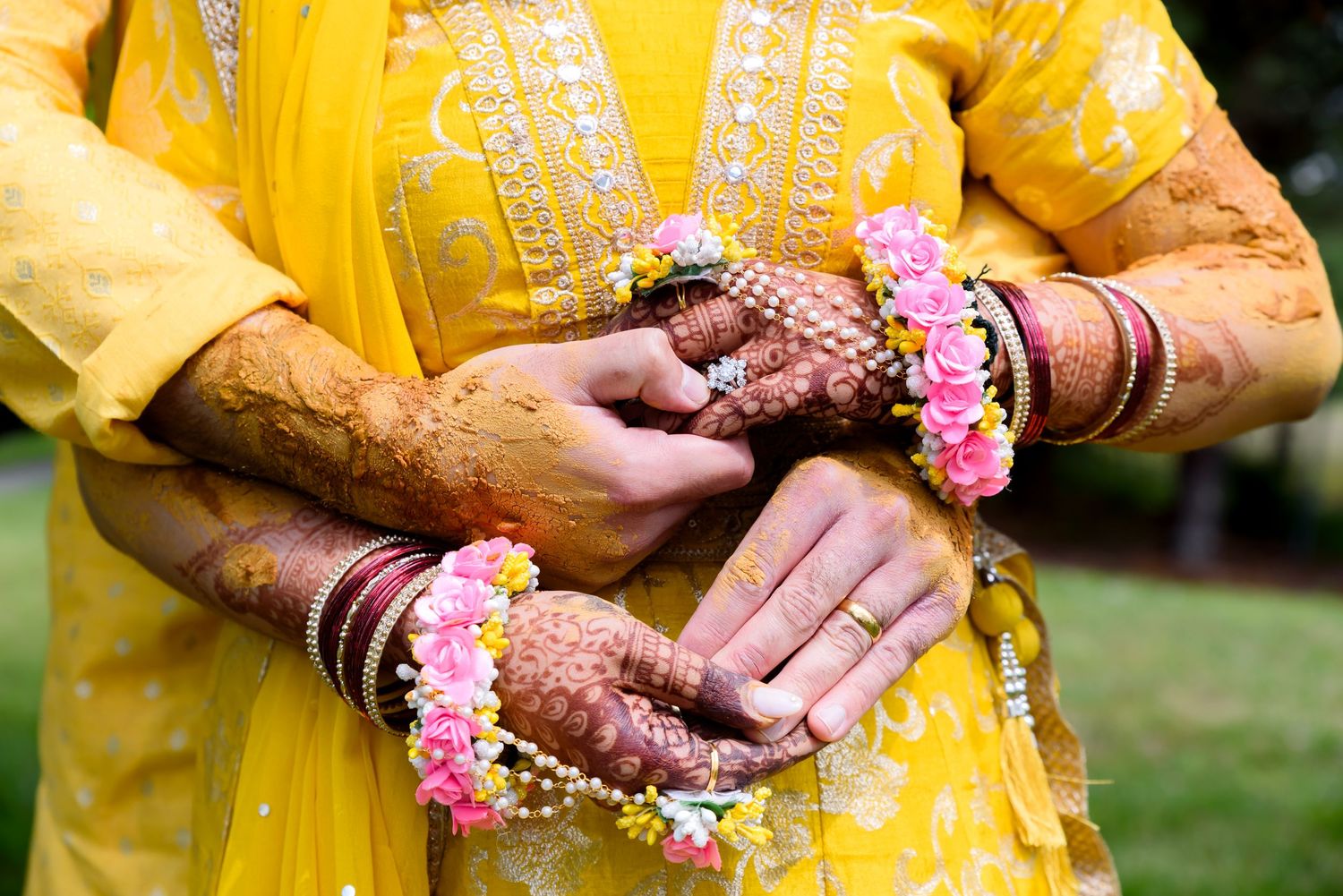 Close-up of Indian bride in yellow salwar with henna hands adorned with floral bangles and colorful chura bracelets.
