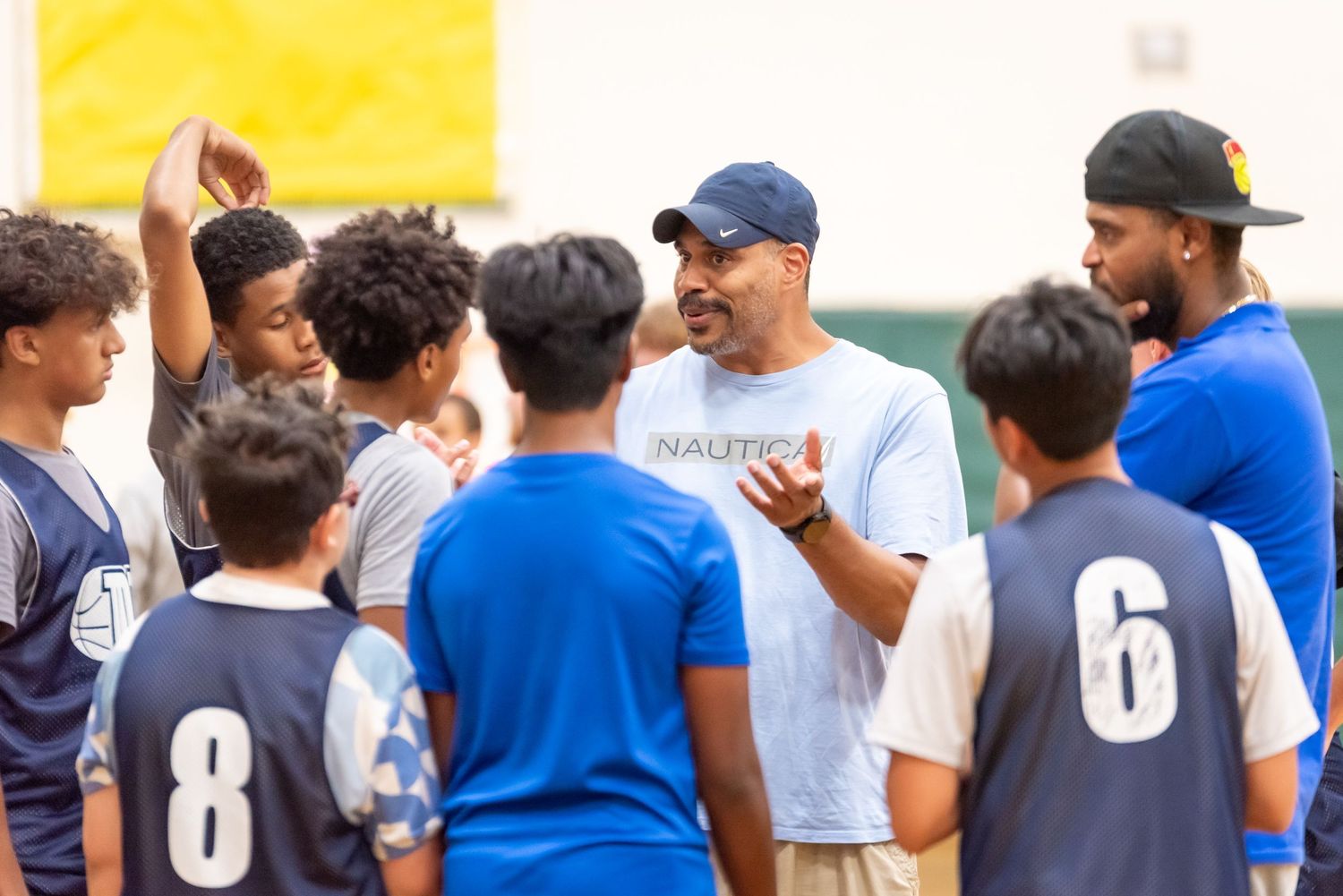 Coach instructs youth baseball players during team practice session on outdoor field.