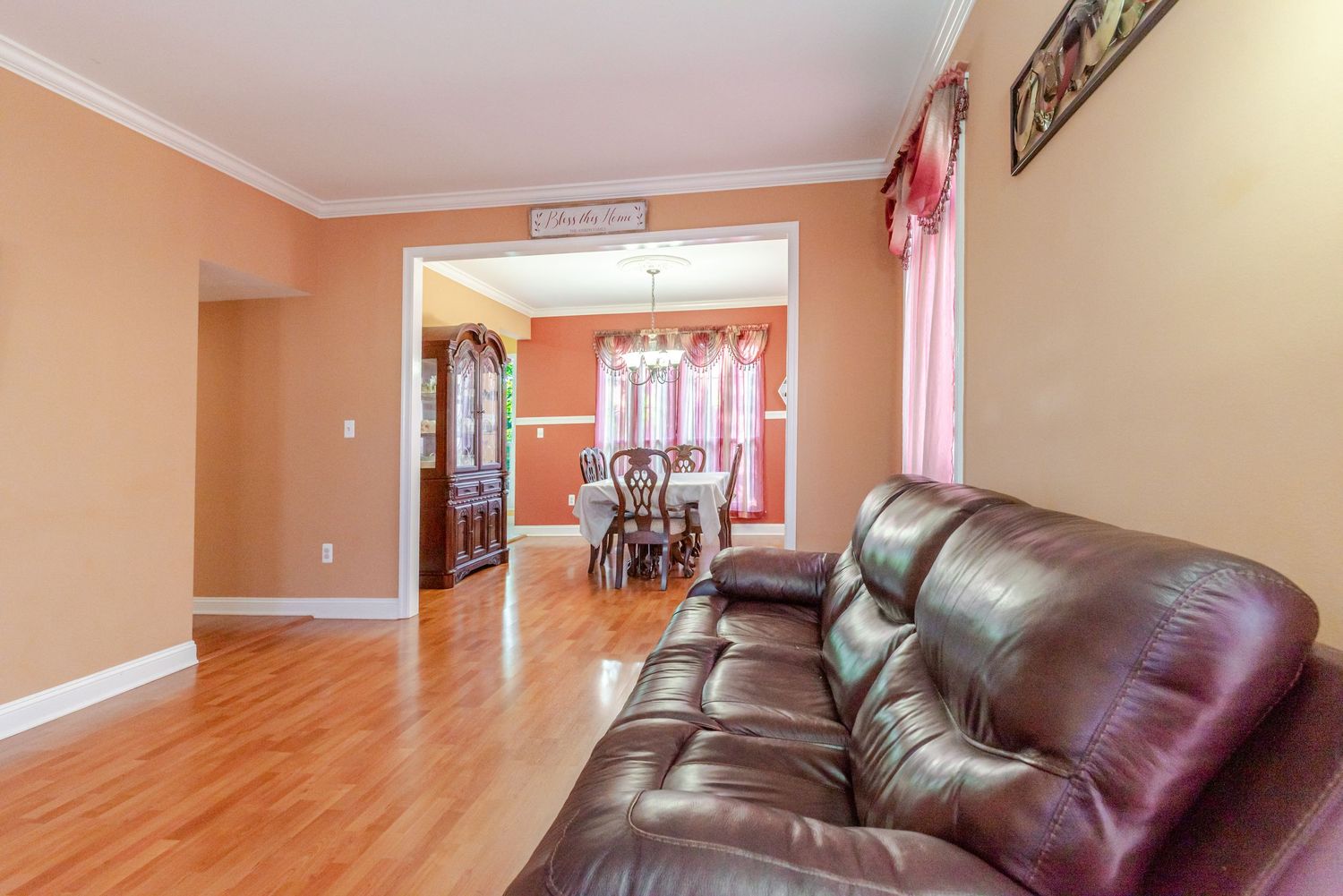 Bright living room with dark brown leather sofa, hardwood floors, crown molding, and open view to formal dining room.