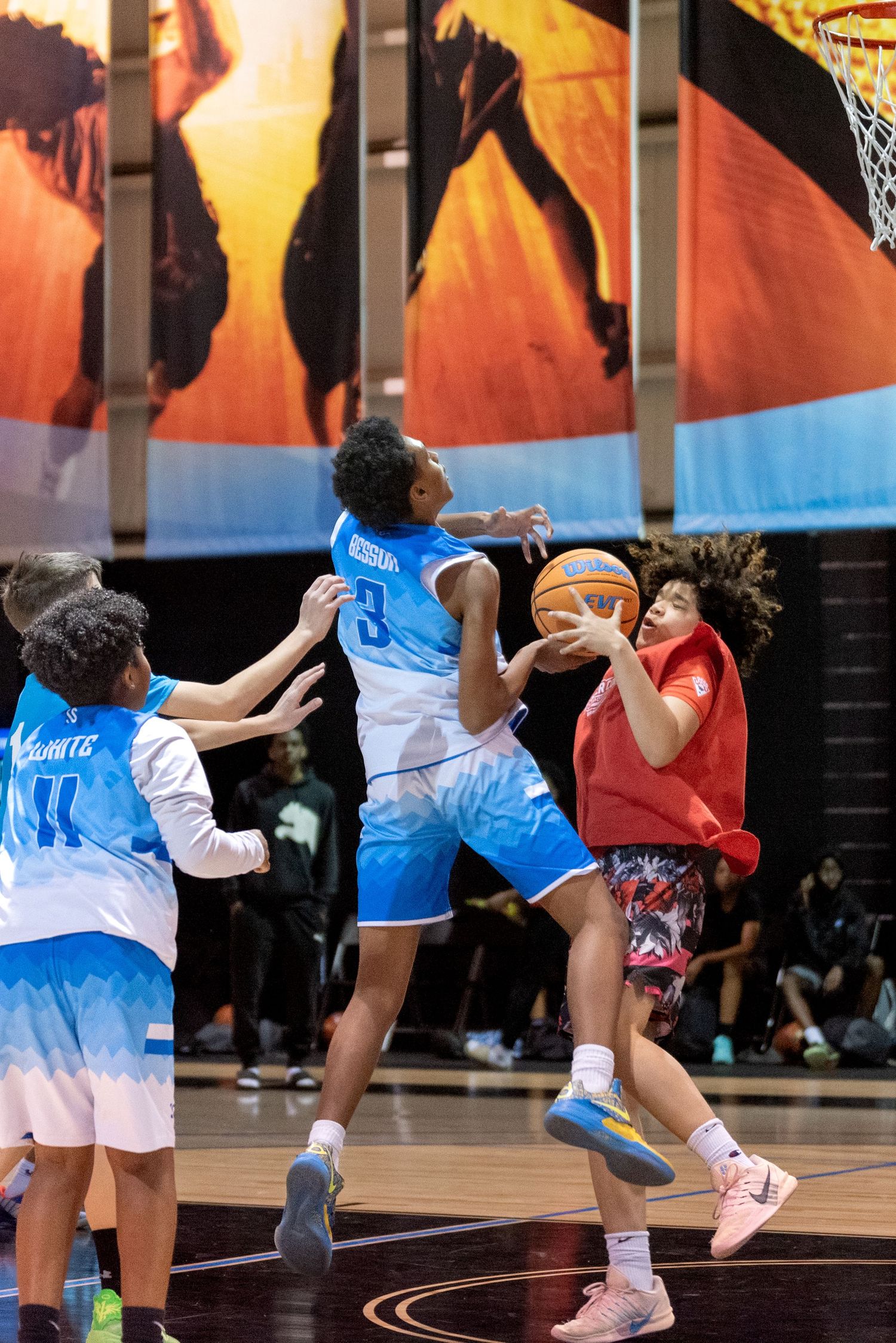 Youth basketball players compete in an intense indoor game, with one player driving to the basket against defenders.