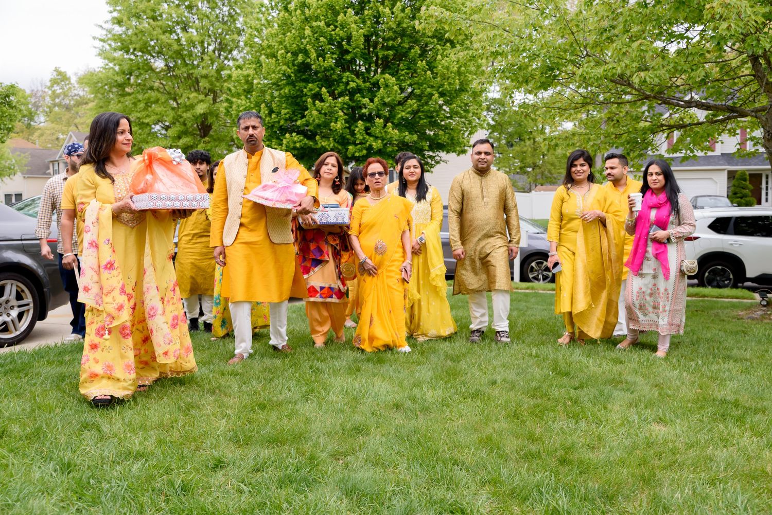 A joyful Indian family dressed in vibrant yellow traditional attire celebrates outdoors on green grass during a festive ceremony.