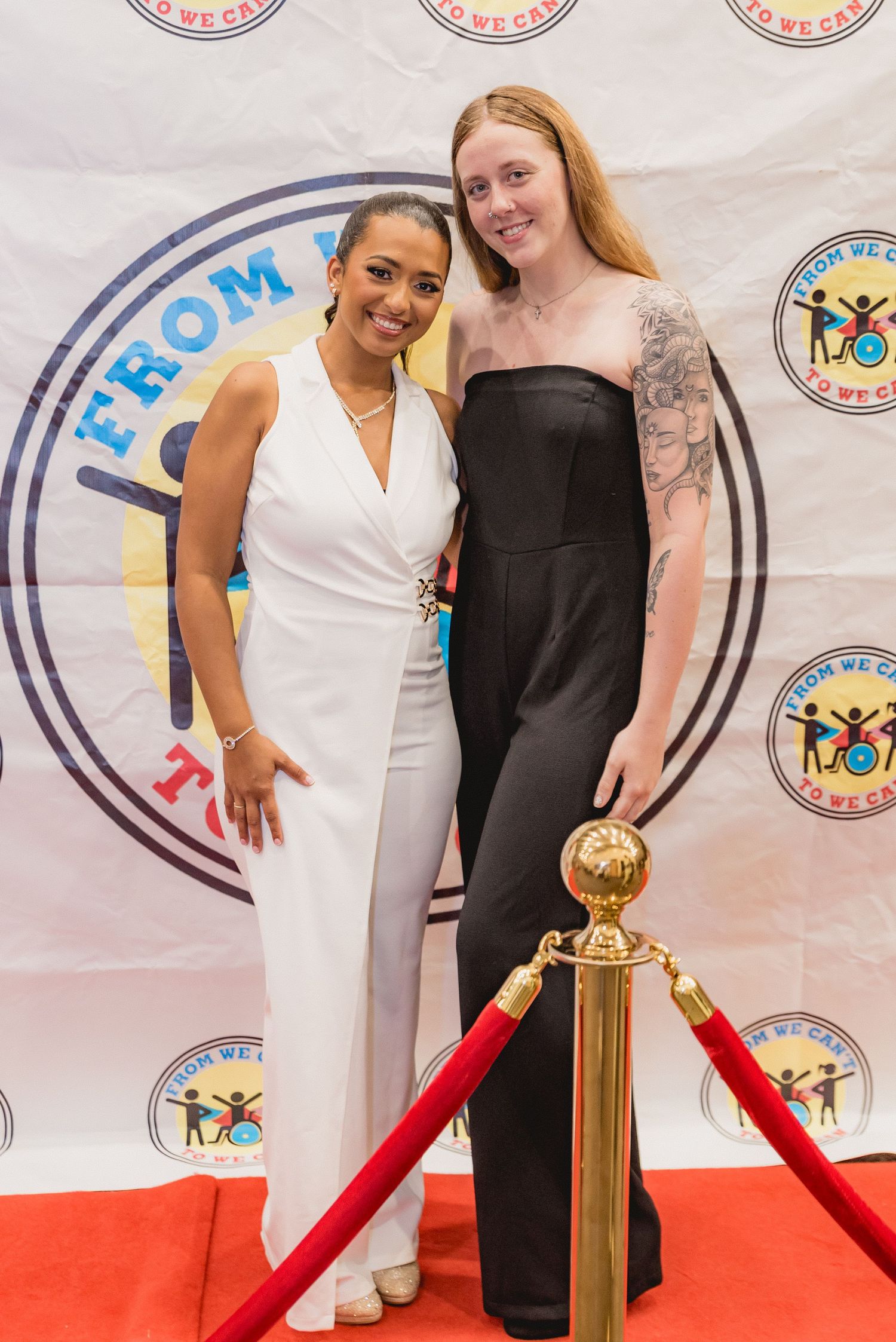 Event guests pose on red carpet near gold stanchion posts at formal gathering.