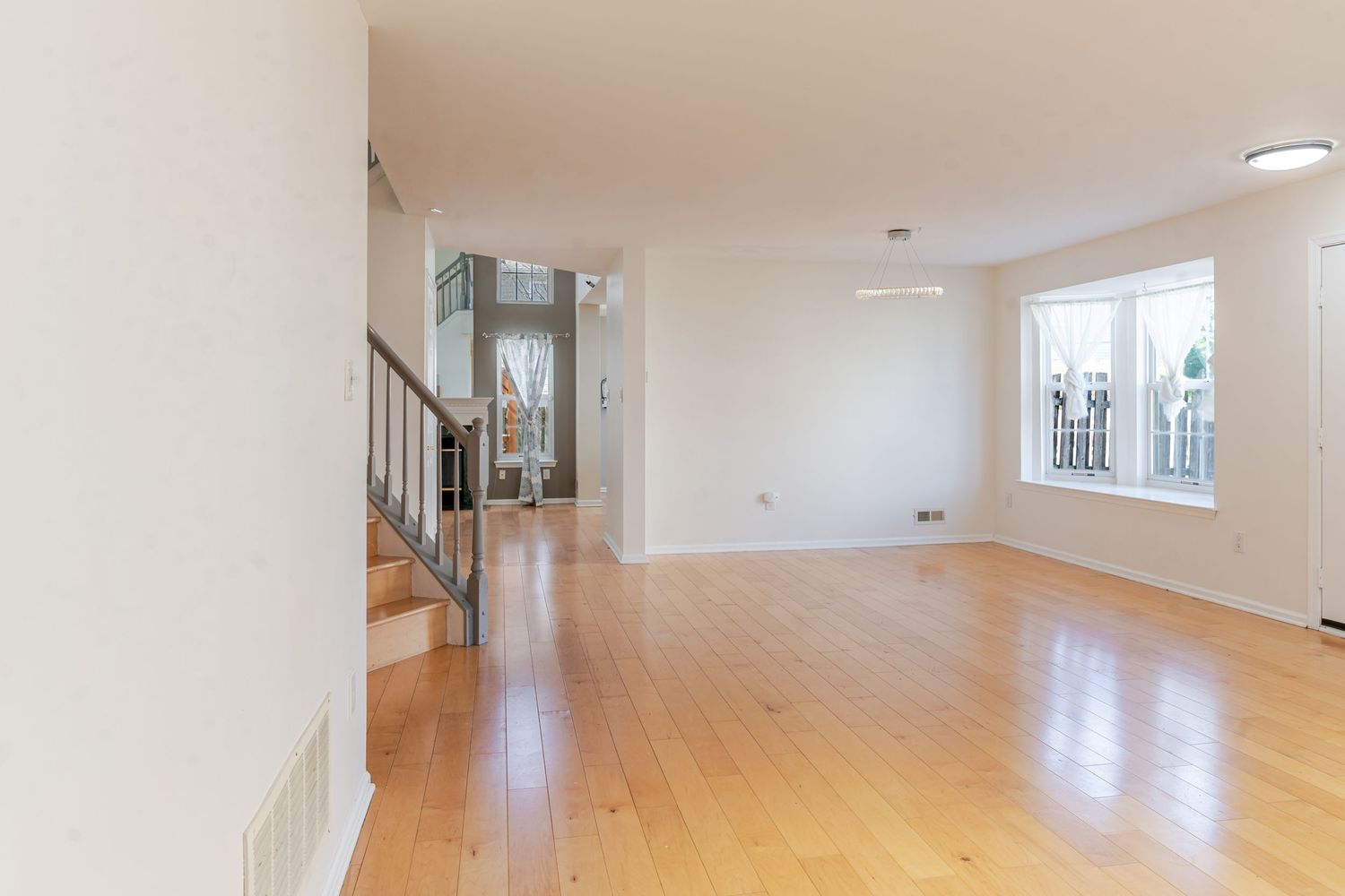 Bright empty living room with hardwood floors, white walls, staircase, and natural light from a window.