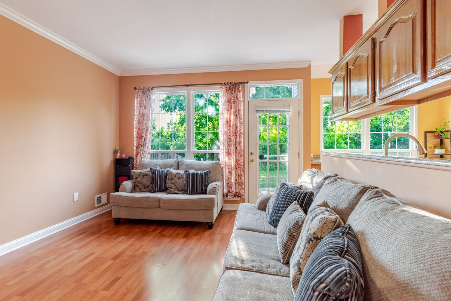 Bright living room with hardwood floors, gray sofas, large windows, and warm peach walls with wood trim accents.