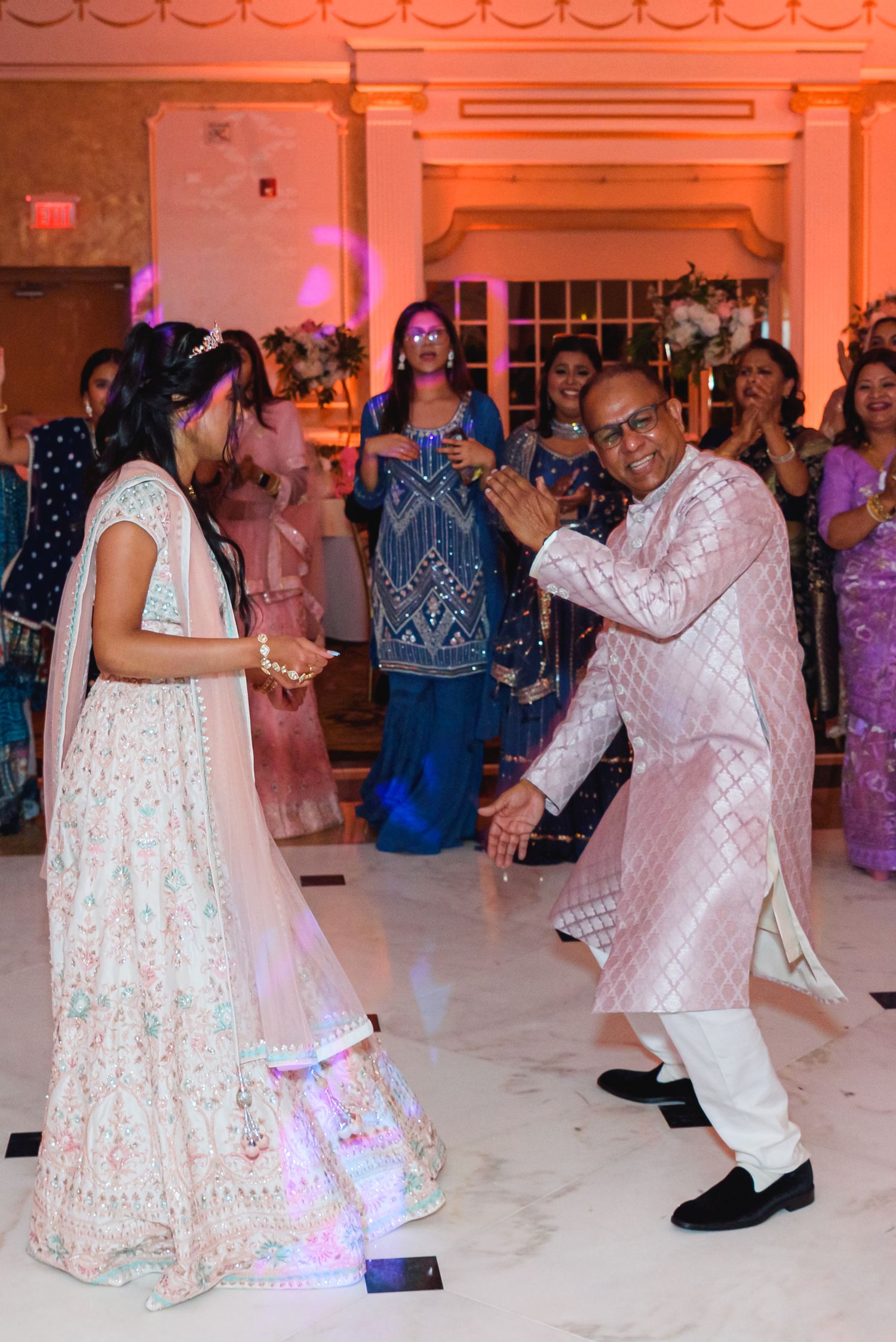 Wedding guests dancing in traditional Indian attire at an elegantly lit reception venue.