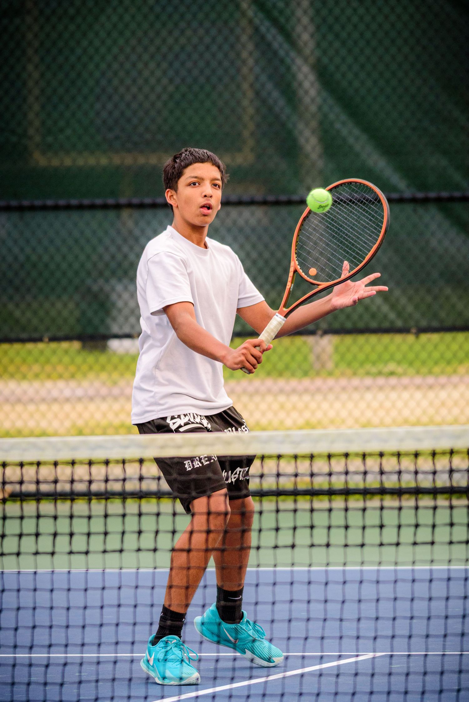 Tennis player in white shirt and shorts prepares to hit a tennis ball on outdoor court.