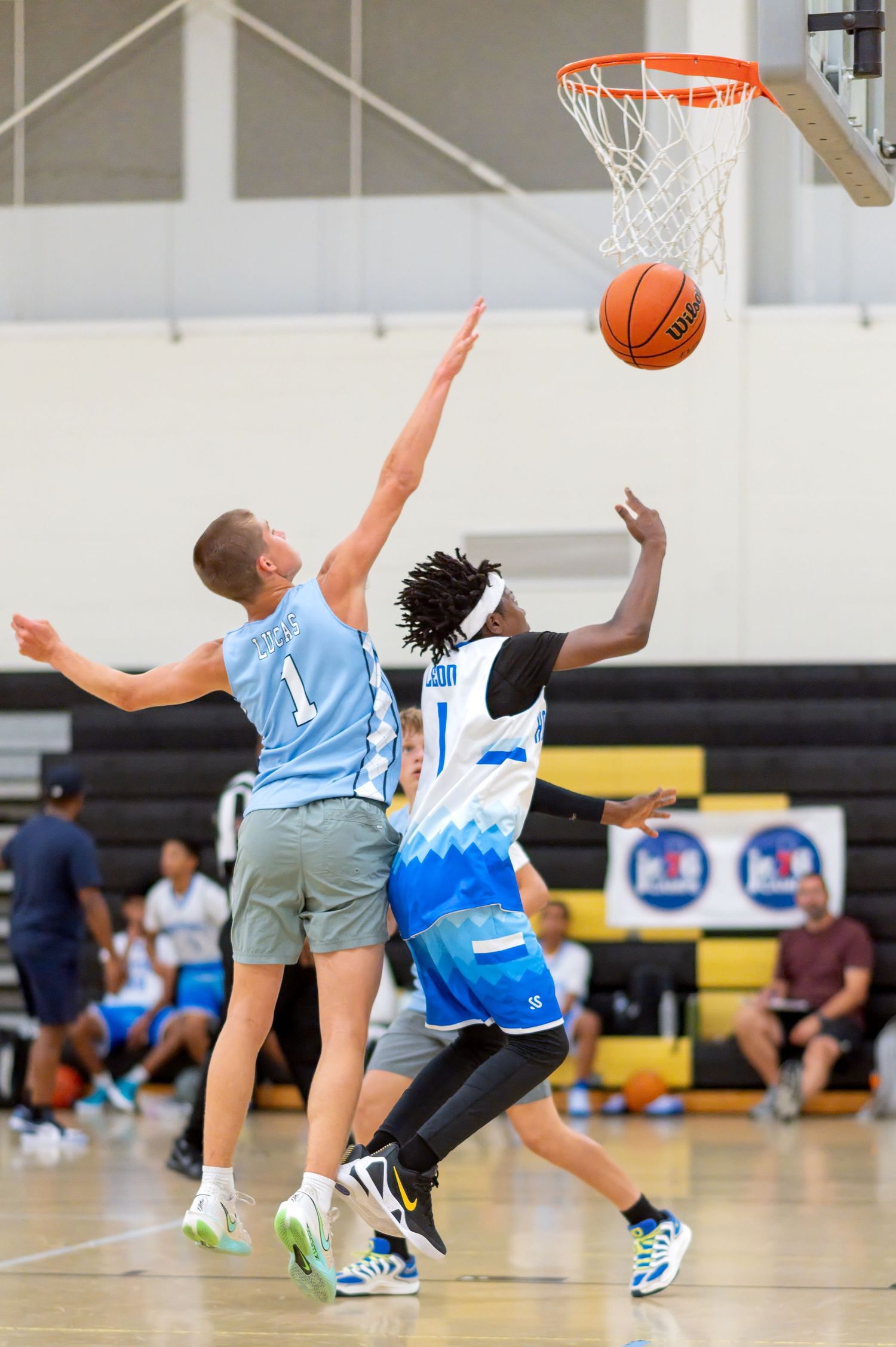 Two basketball players compete for a layup shot during an indoor youth basketball game, with player #1 in blue defending.