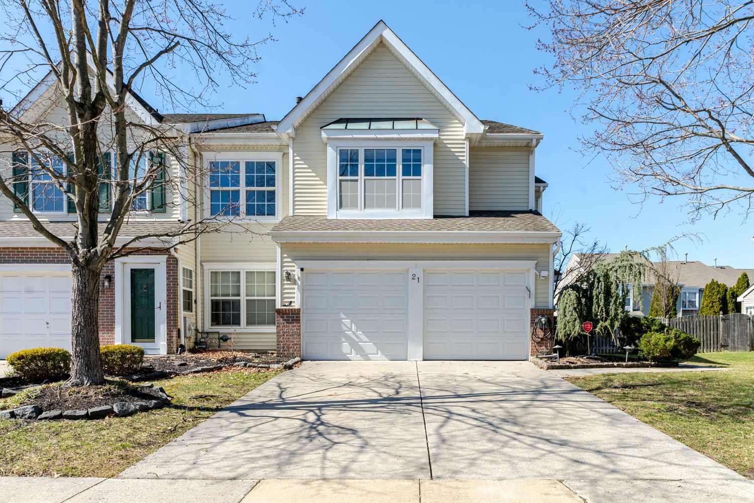Two-story suburban home with white siding, double garage, brick accents, and manicured landscaping on a sunny day.