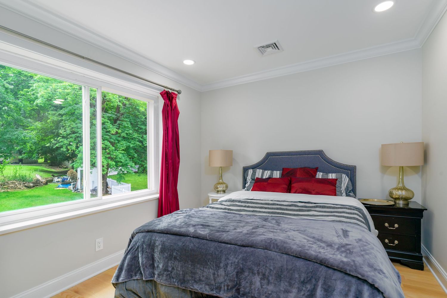 Modern bedroom with gray bedding, red accents, and large windows overlooking greenery.