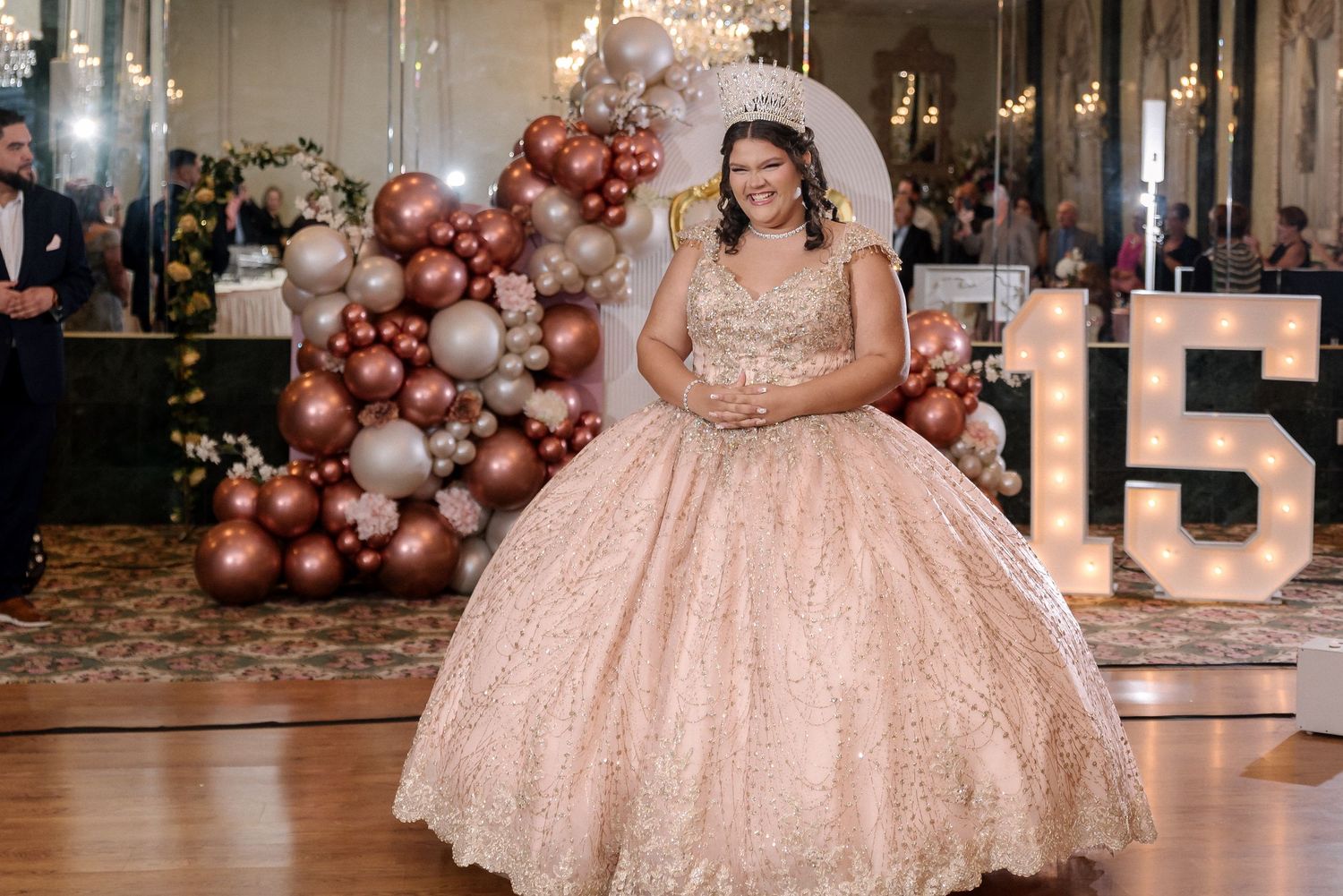 Elegant ballroom setup with rose gold balloon arches and crystal chandeliers for a special celebration.