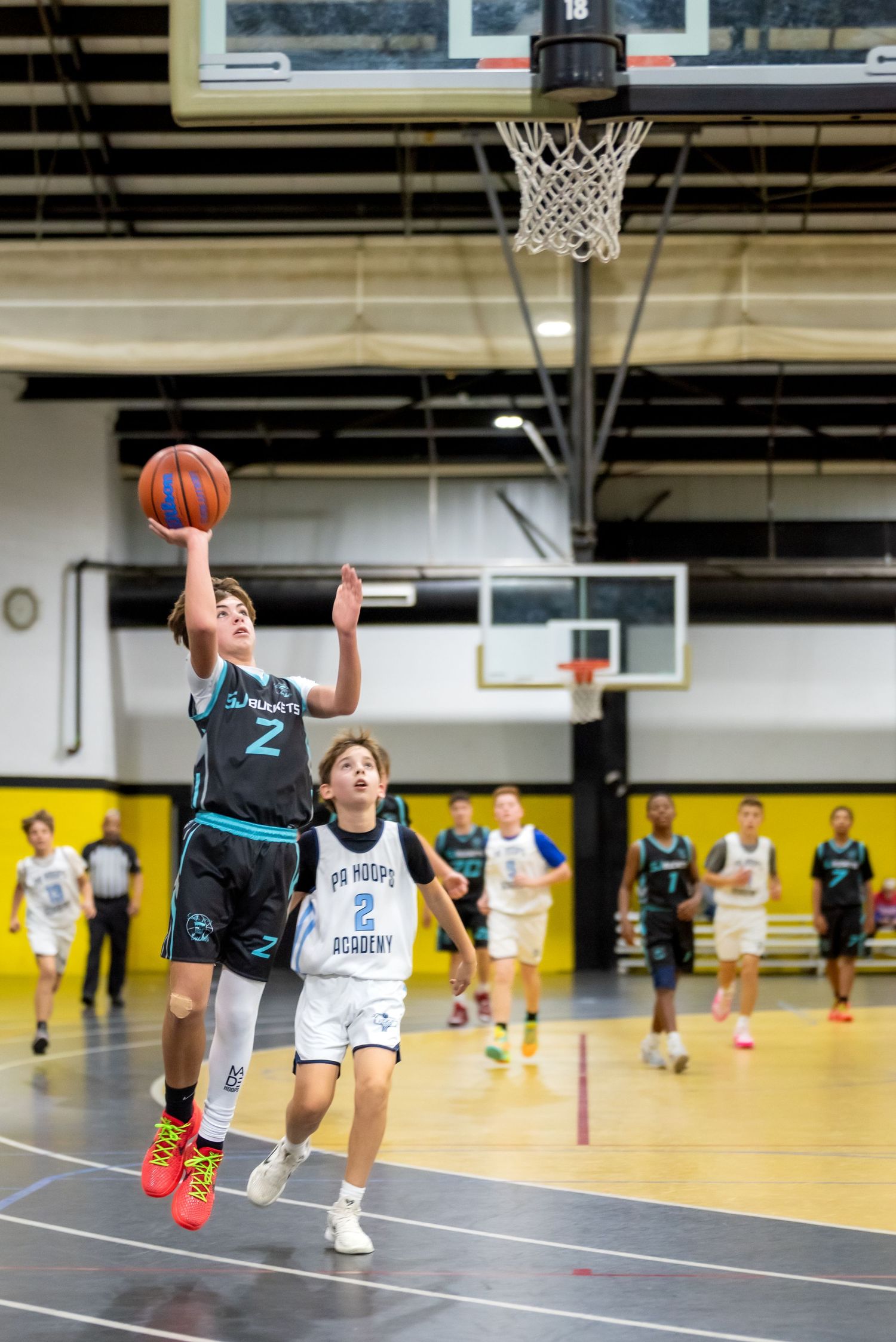 Young basketball player in black jersey #2 leaps for a layup during an indoor youth basketball game.
