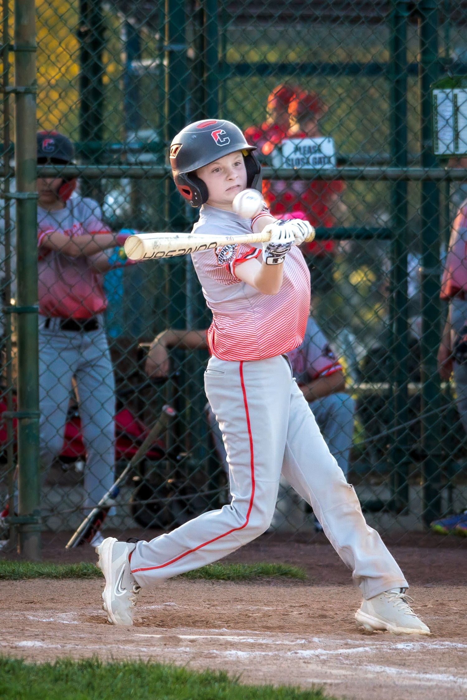 Young baseball player in red and white uniform swings bat during little league game.