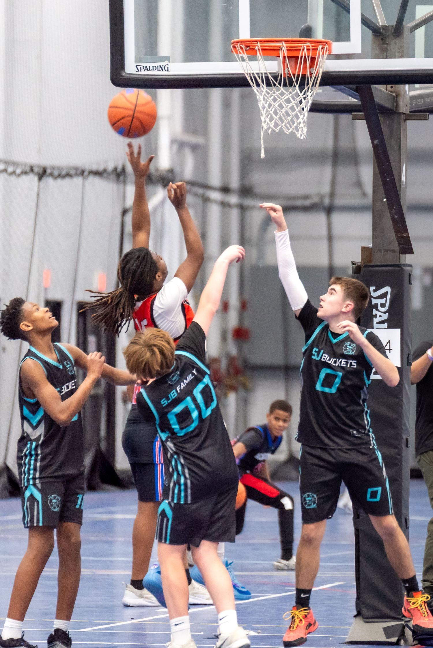Youth basketball players compete in an indoor game, with one player shooting near a Spalding hoop.