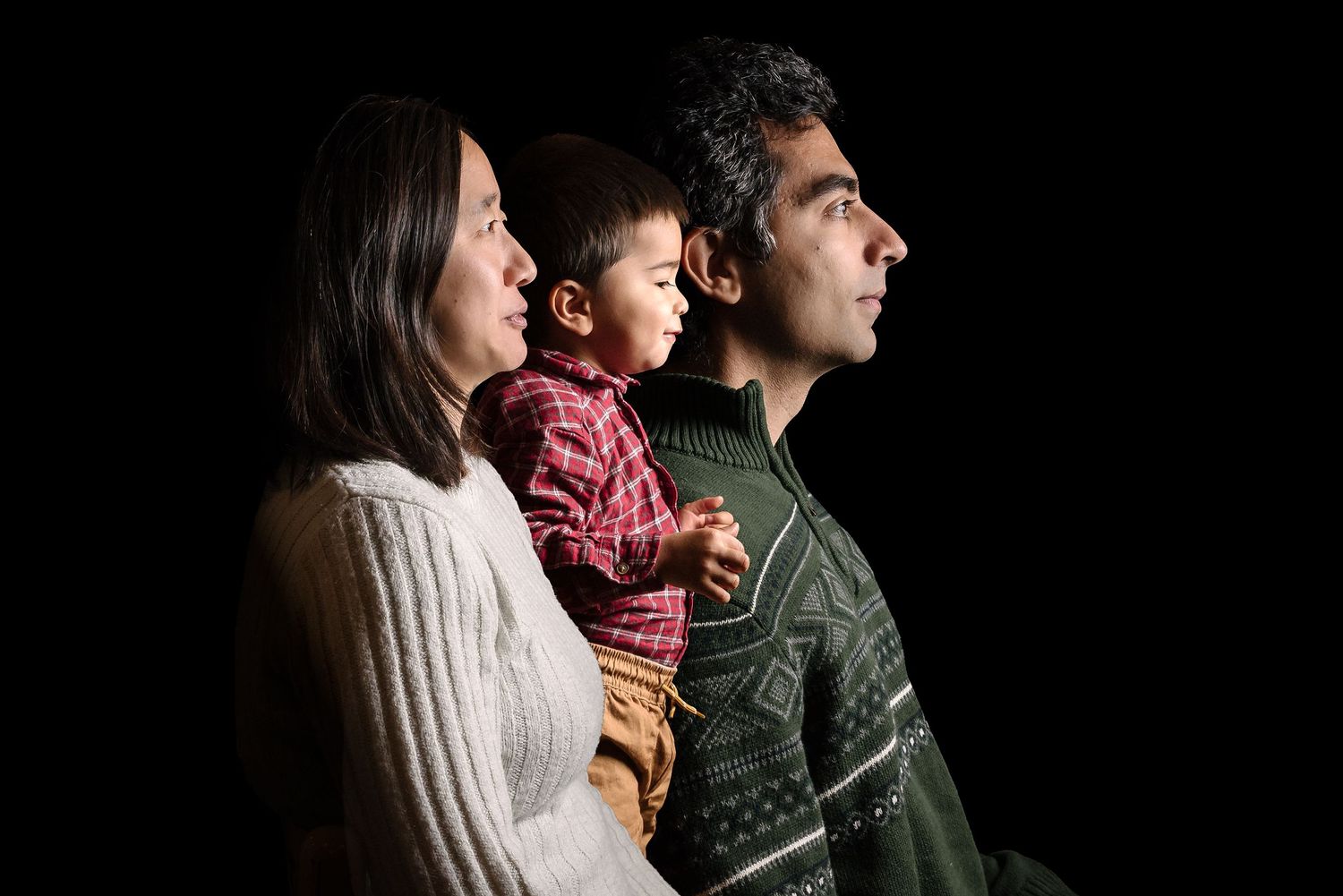 A family in profile stands together wearing winter clothing while looking off into the distance.