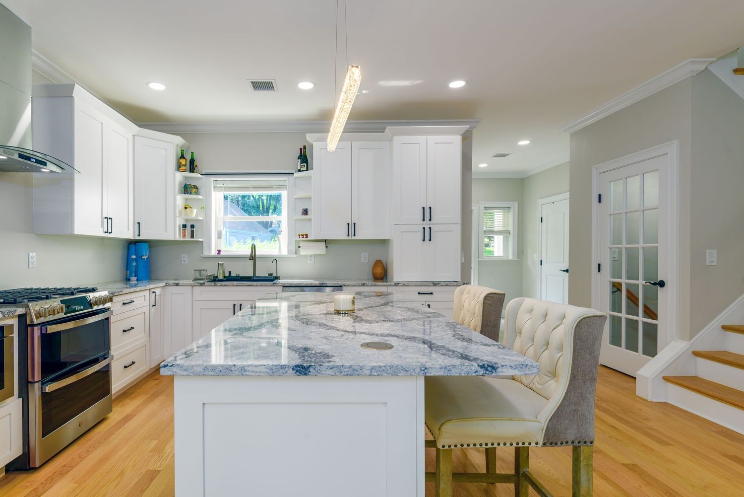 Sleek white kitchen with marble countertops, center island, and modern appliances.