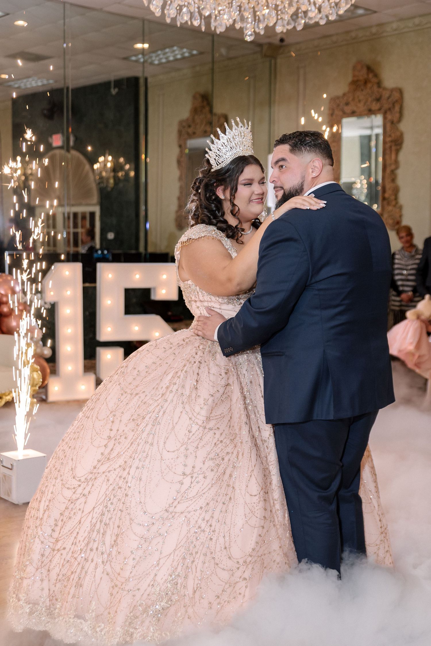 A romantic dance moment on a fog-covered dance floor under sparkling chandeliers.