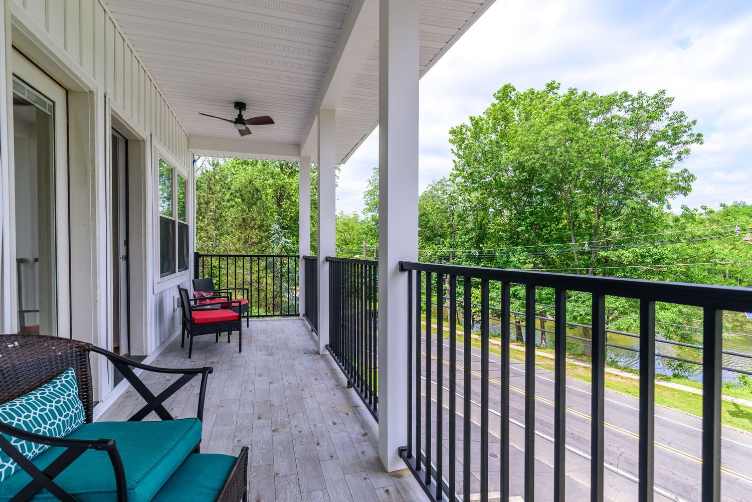 Spacious covered porch with black railings and ceiling fans extending along the front of the house.