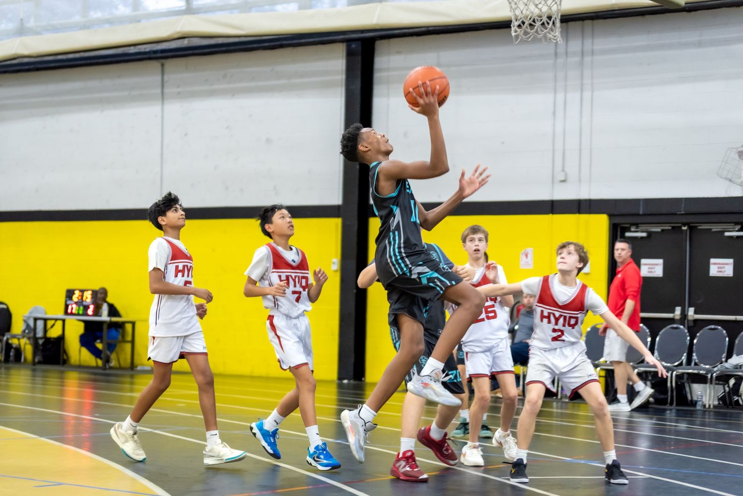 Young basketball player attempts a layup against defenders during a youth indoor basketball game.