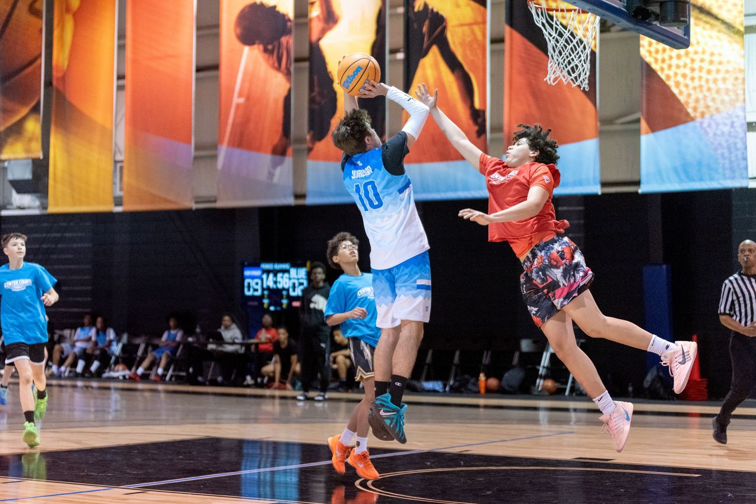 Youth basketball players compete in a layup attempt during an indoor game, wearing blue and red uniforms.