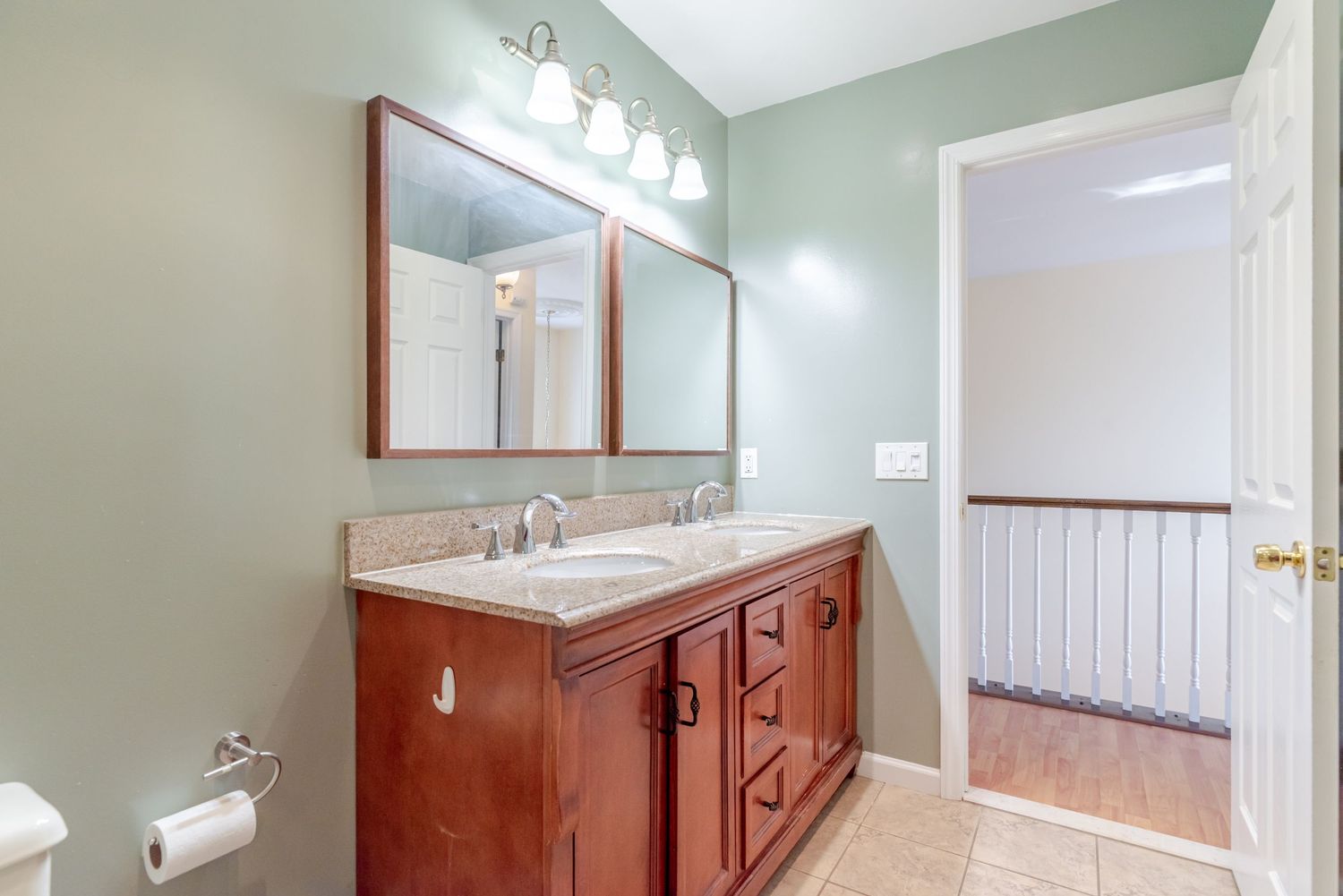 Bathroom with cherry wood double vanity, granite countertop, dual sinks, large mirror, and light tile flooring.