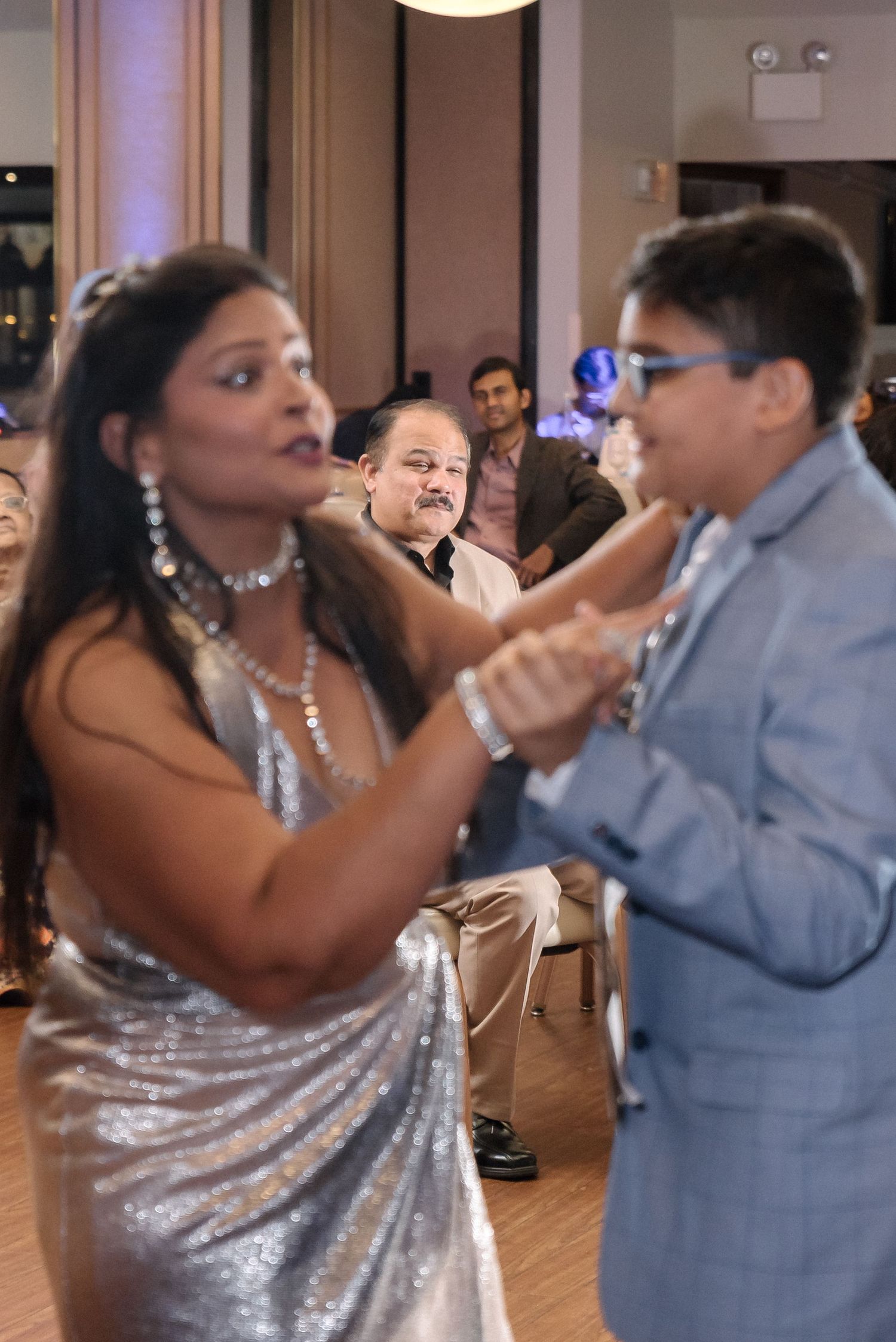 Dancers in formal attire perform energetic moves at an indoor celebration.