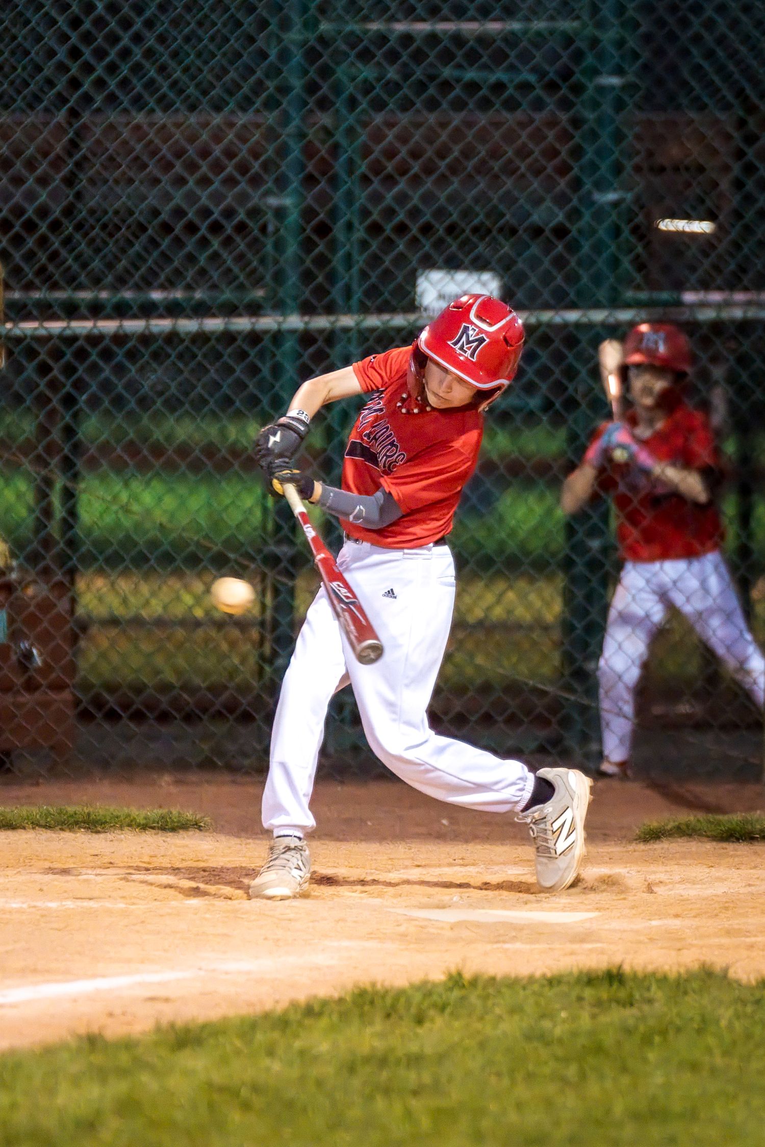 Young baseball player in red uniform swings bat at incoming pitch during a youth league game.