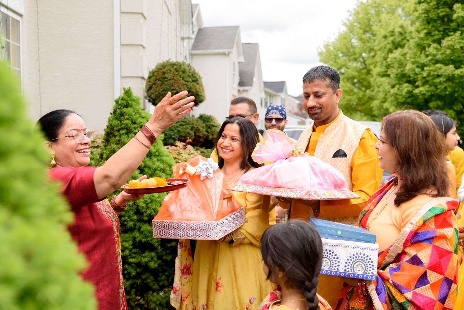 Colorful Indian wedding ceremony with guests in traditional attire exchanging gifts outdoors amid lush green surroundings.