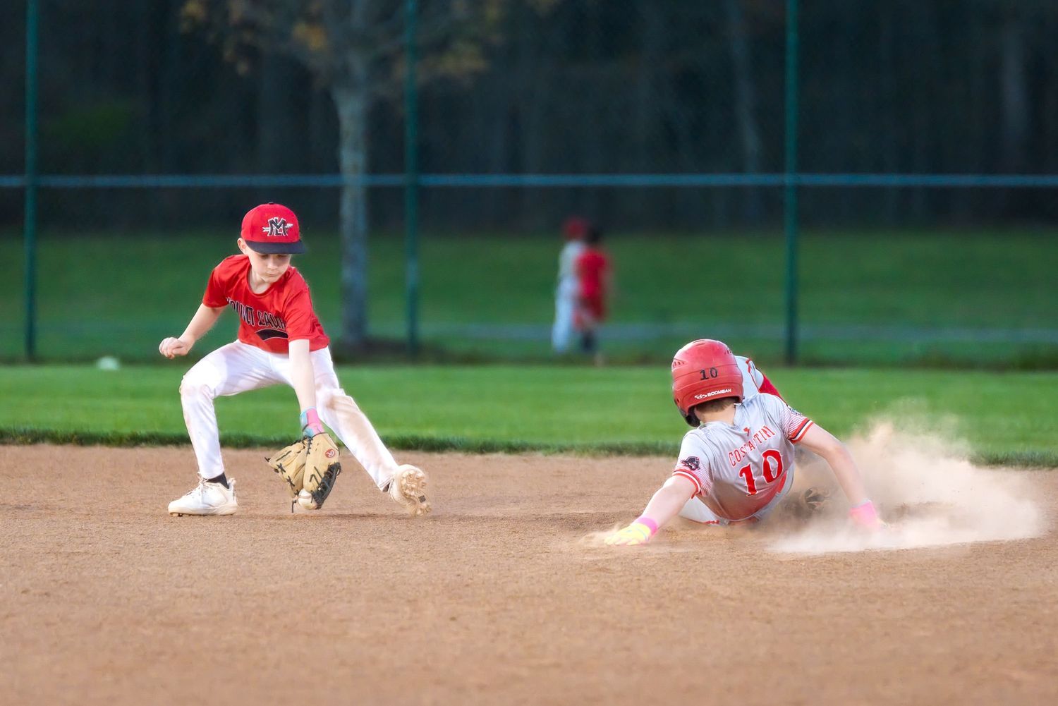 Little league baseball player slides into second base as fielder attempts tag.