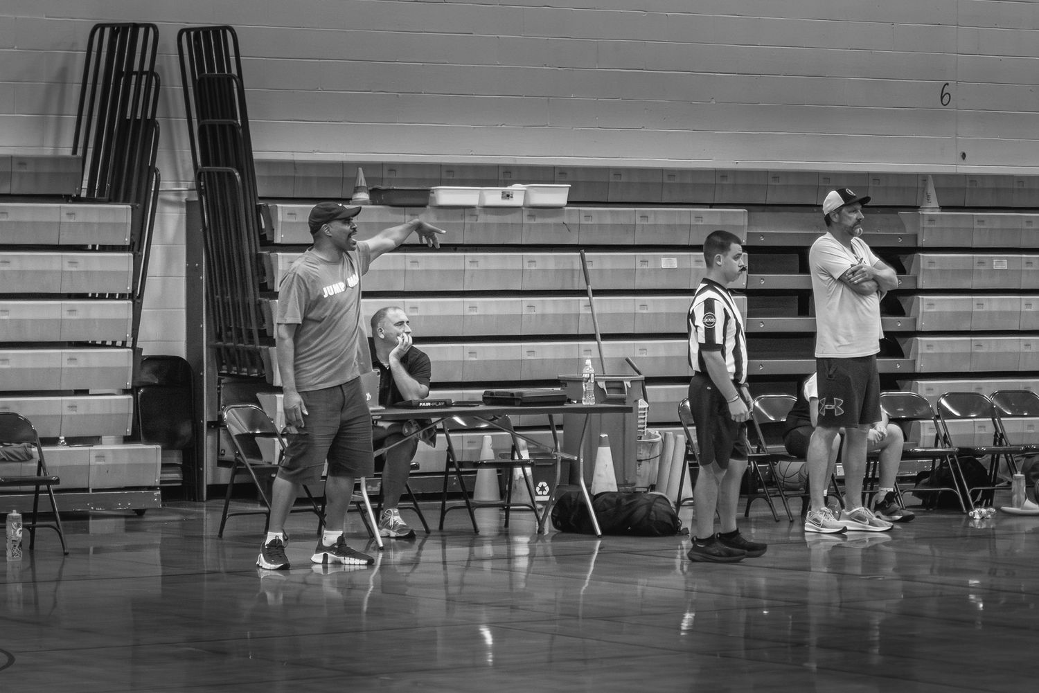 People gather in a gymnasium with bleachers during what appears to be a sports practice or training session in black and white.