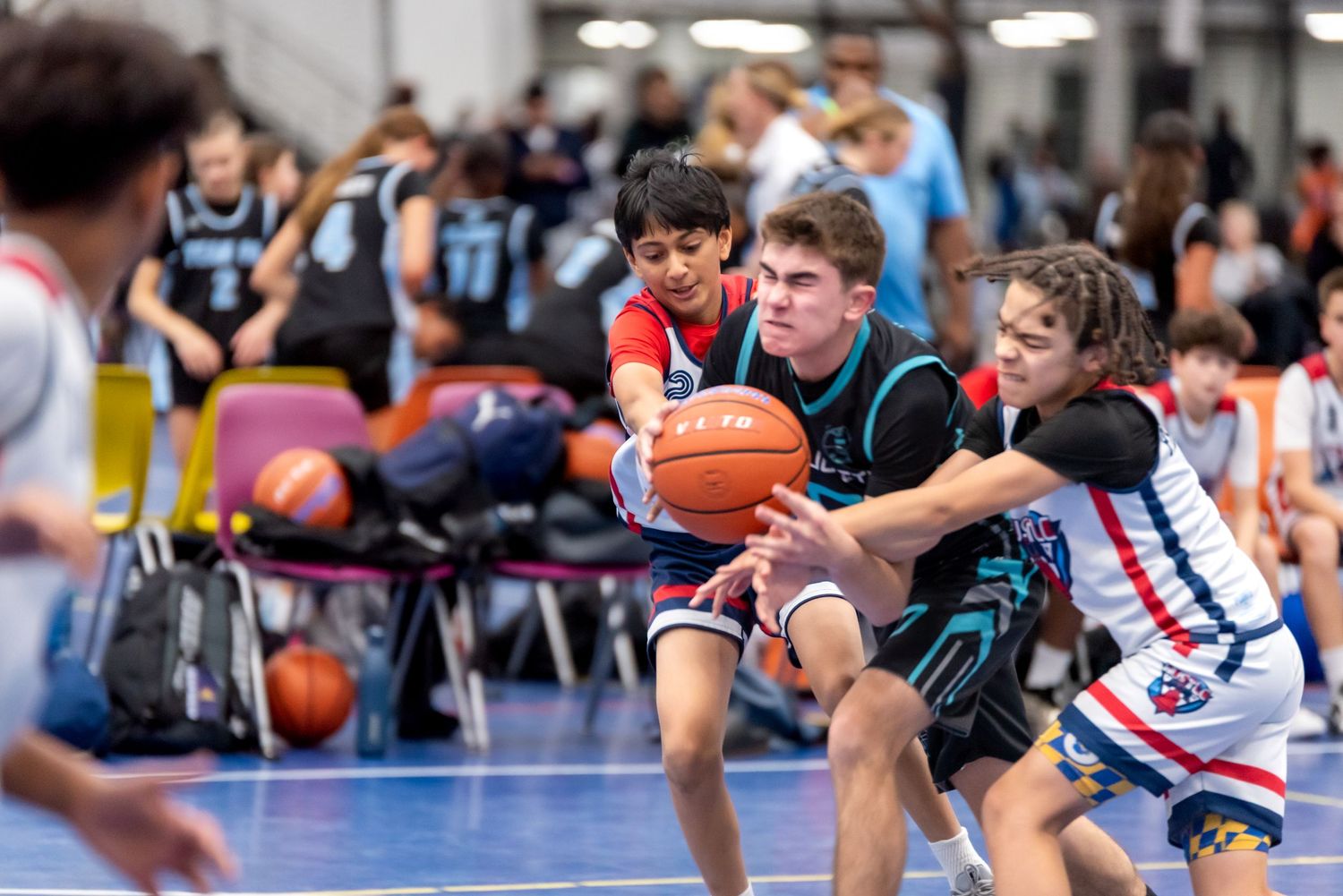 Young basketball players compete for the ball during an intense indoor youth basketball game.