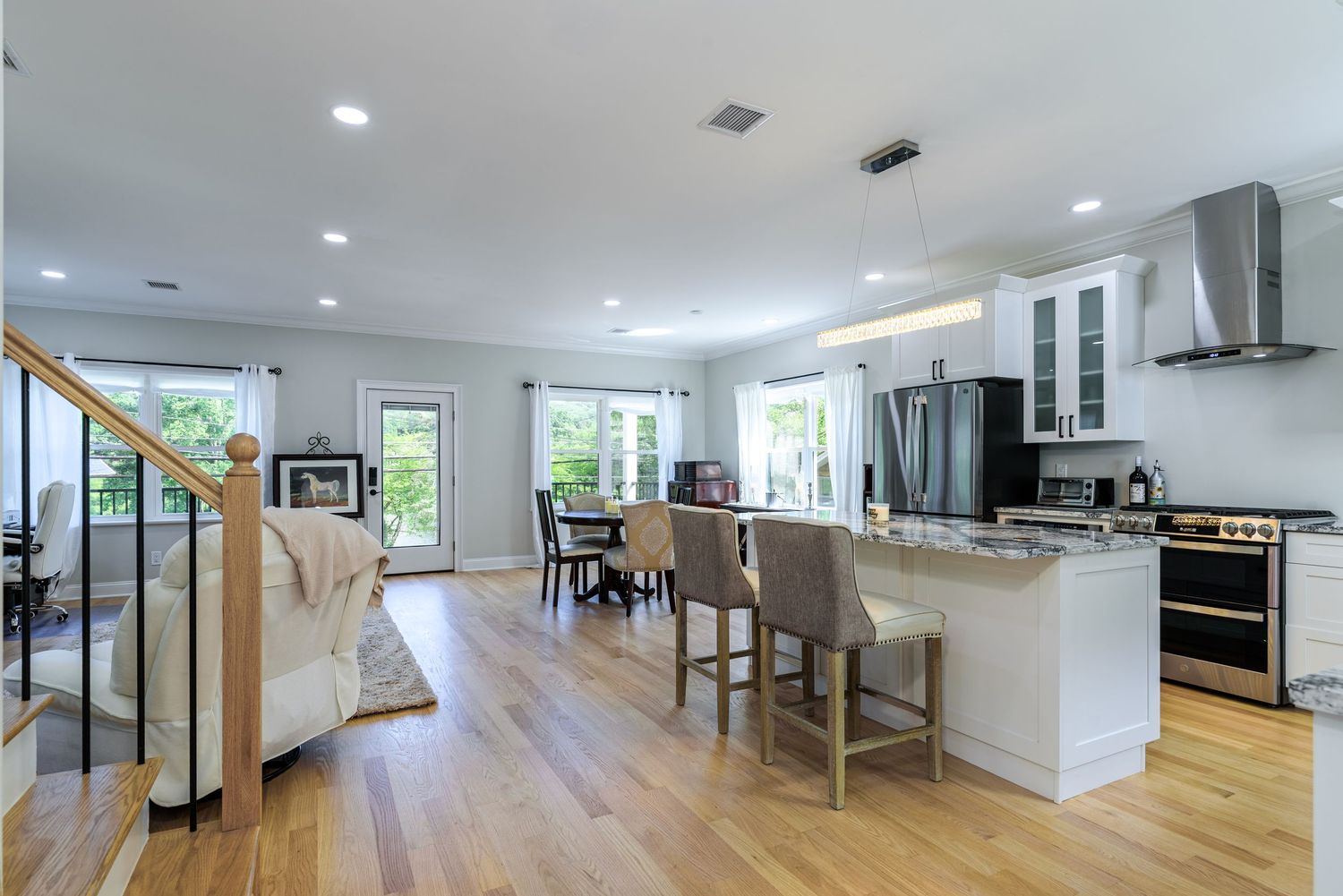 Bright modern kitchen and dining area with white cabinets and stainless steel appliances.