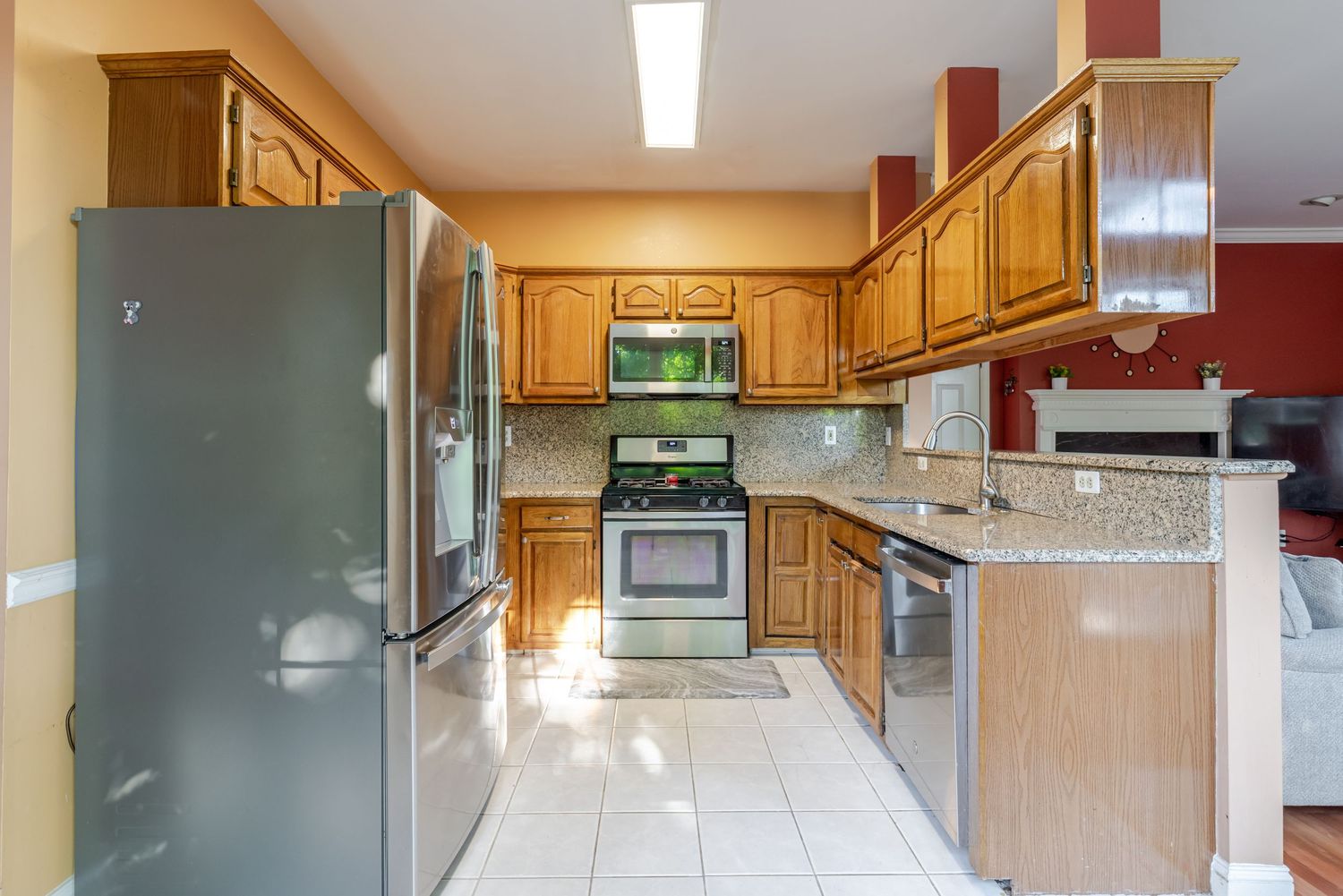 Spacious kitchen featuring oak cabinets, stainless steel appliances, granite countertops, and white tile flooring.