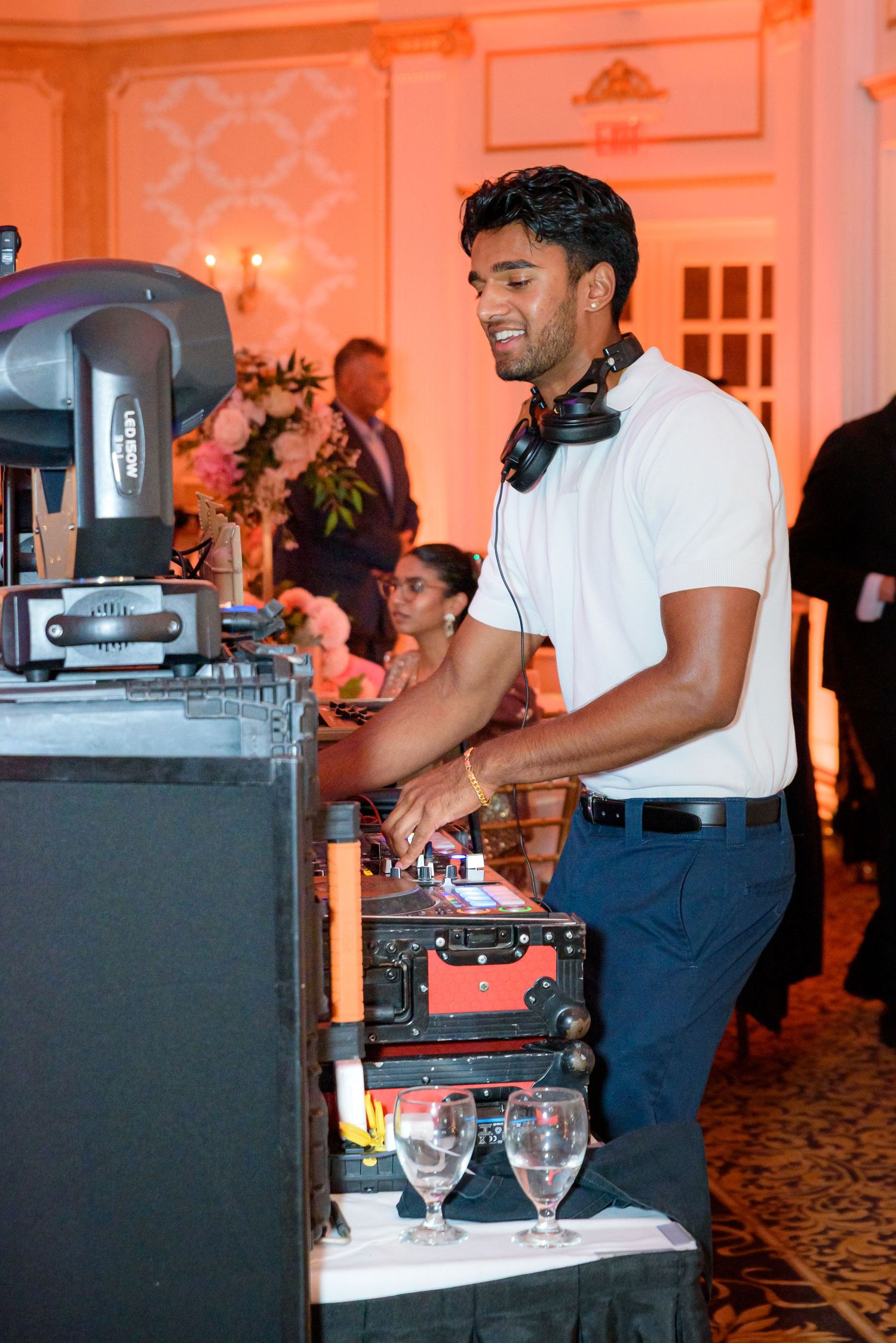 DJ equipment setup at an elegant event venue with warm orange lighting and professional audio gear.