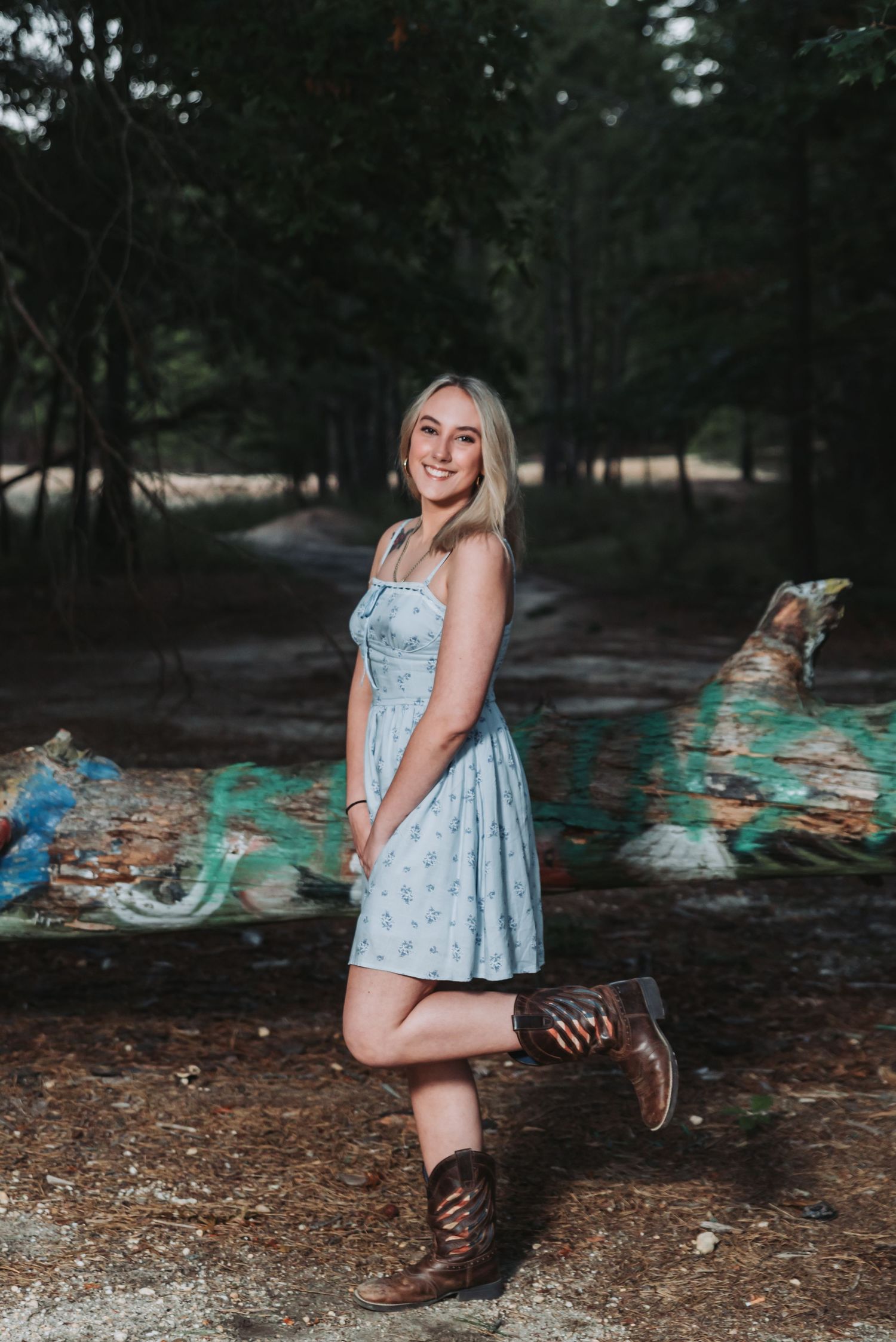 A series of outdoor portrait photos showing someone in a light blue dress and brown boots sitting on graffiti-covered rocks.